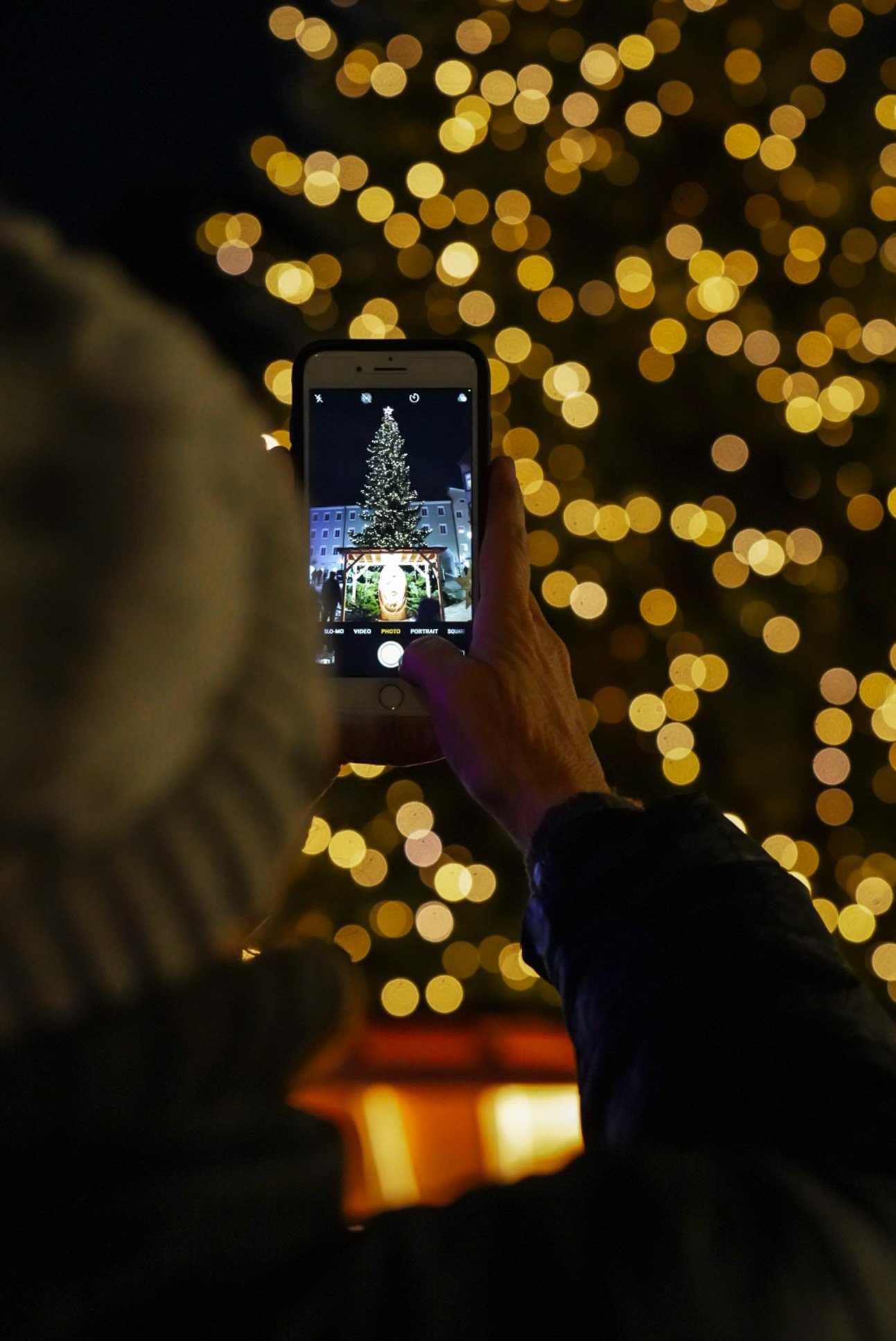 A woman takes a photo of the town Christmas tree in Rattenberg, Austria, on Dec. 24, 2021. Standing 14 meters high, the tree dwarfs the nearby buildings with ease. © Merit Davey 2021.