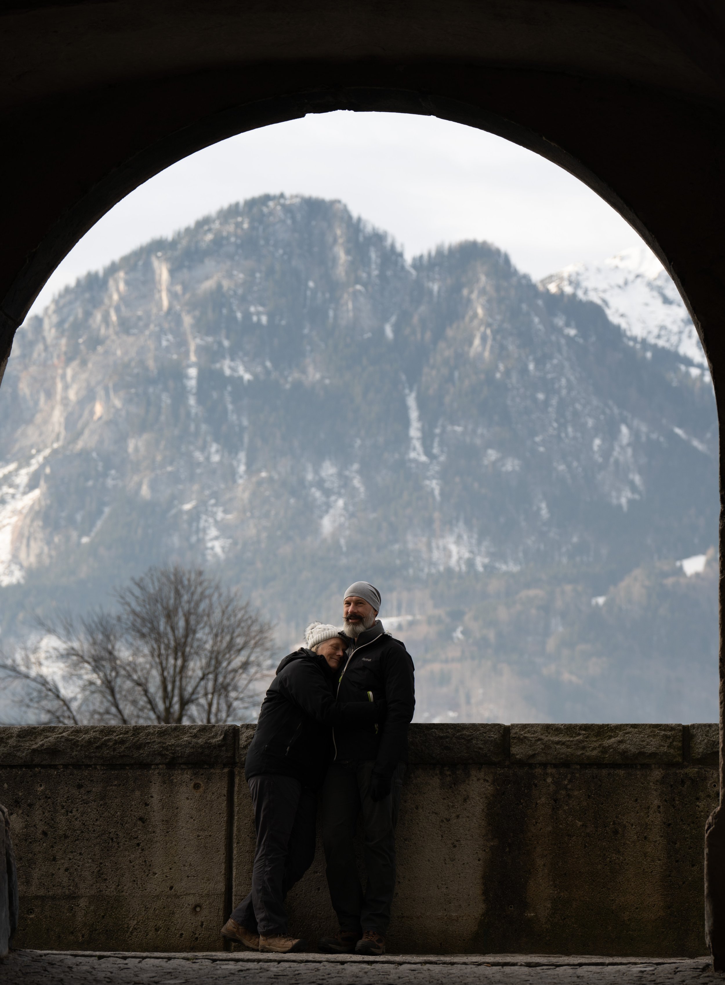 A man and his wife stand for a portrait during their morning walk in Rattenberg, Austria, on Dec. 21, 2021. The idyllic backdrop of the Alps make it difficult not to feel life's worries dissipate. © Merit Davey 2021.