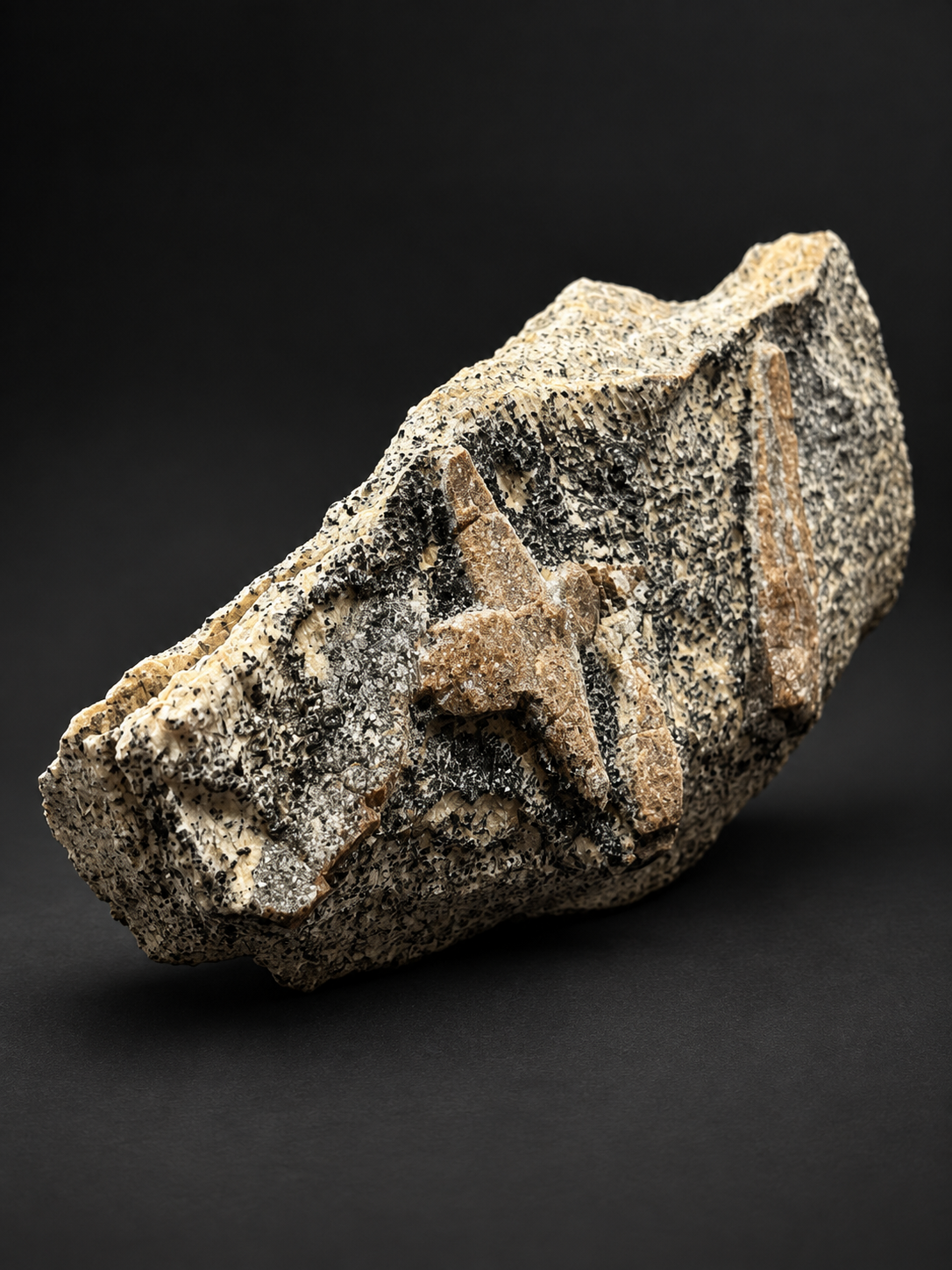 Russian staurolite on schist showing a cross-shaped brown crystal formation beside a long prismatic crystal on densely black-speckled cream matrix.