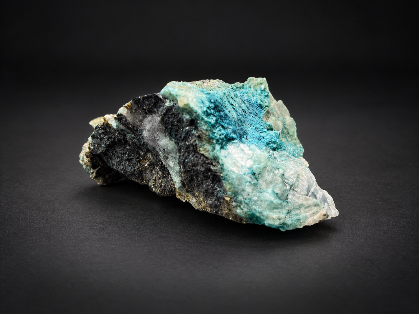 ark metallic-looking matrix, translucent white crystalline sections, and aqua-blue mineralization along the upper edge.