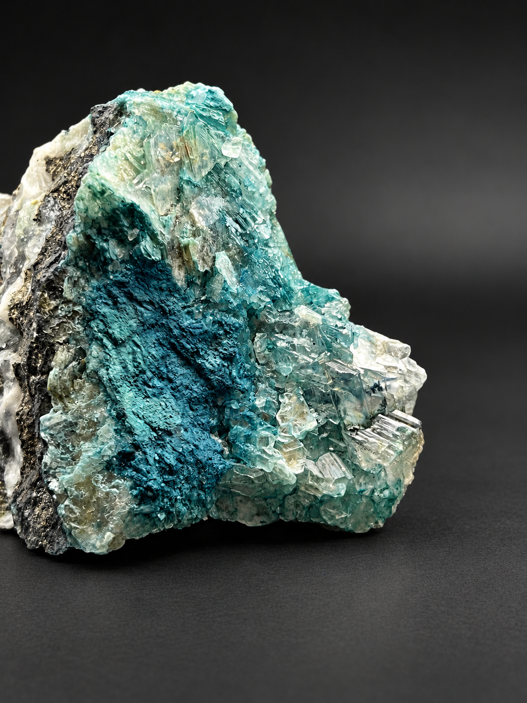 Macro view of vivid turquoise-blue mineralization surrounded by delicate translucent, pale green, and clear bladed crystal clusters.