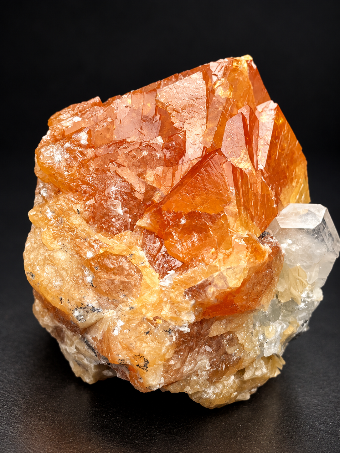 lustrous orange scheelite crystals with pointed dipyramidal formations beside a transparent calcite crystal and creamy muscovite from Sichuan, China.