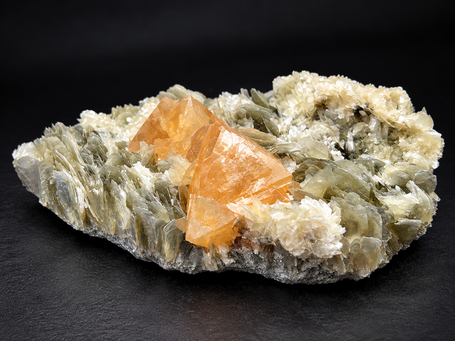 Two golden-orange scheelite crystals with geometric faces nestled among fan-like muscovite blades and pale mica clusters from Mt. Xuebaoding, China.