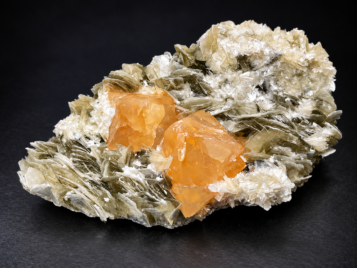 two translucent orange scheelite crystals emerging from cream-colored muscovite rosettes and olive-green mica sheets from Sichuan, China.