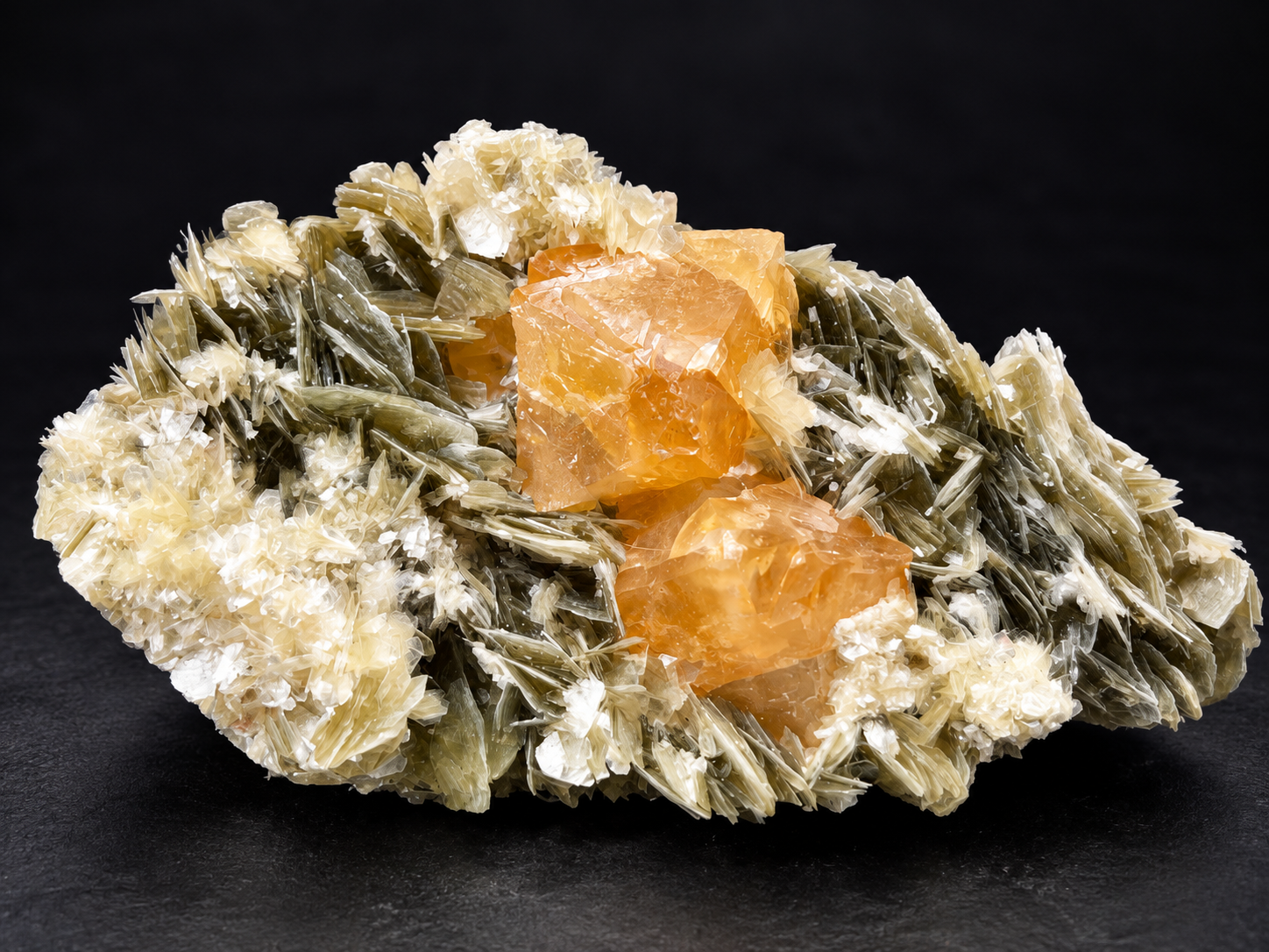 translucent honey-orange scheelite crystals surrounded by olive-green muscovite blades and creamy-white mica rosettes from Mt. Xuebaoding, China.