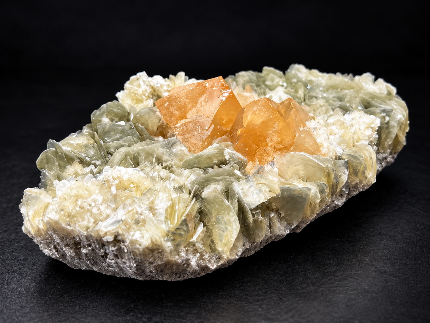 orange scheelite crystals rising from layered olive-green muscovite with delicate white mica formations from Pingwu, Sichuan Province, China.