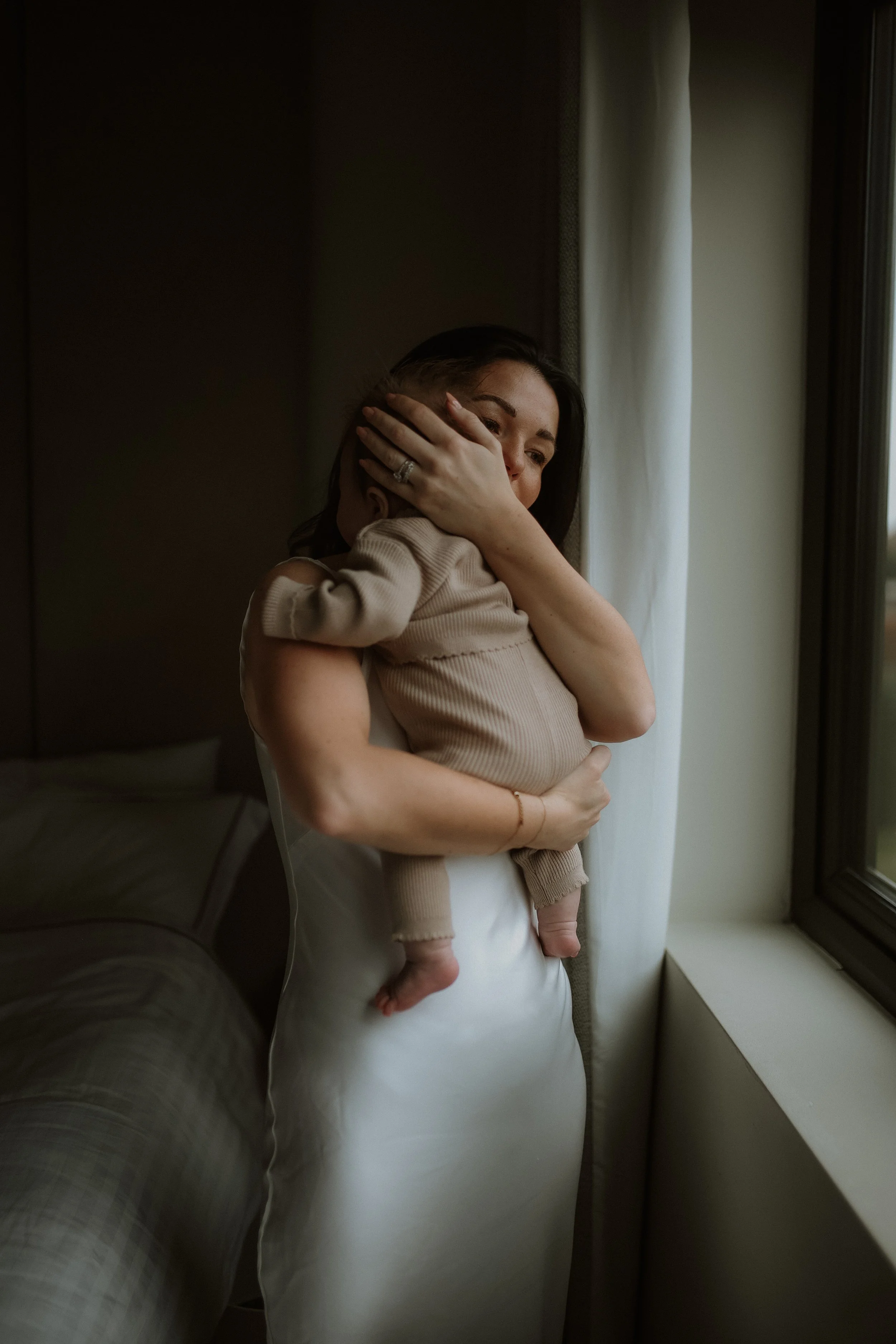 A woman holding a small child next to a window indoors.
