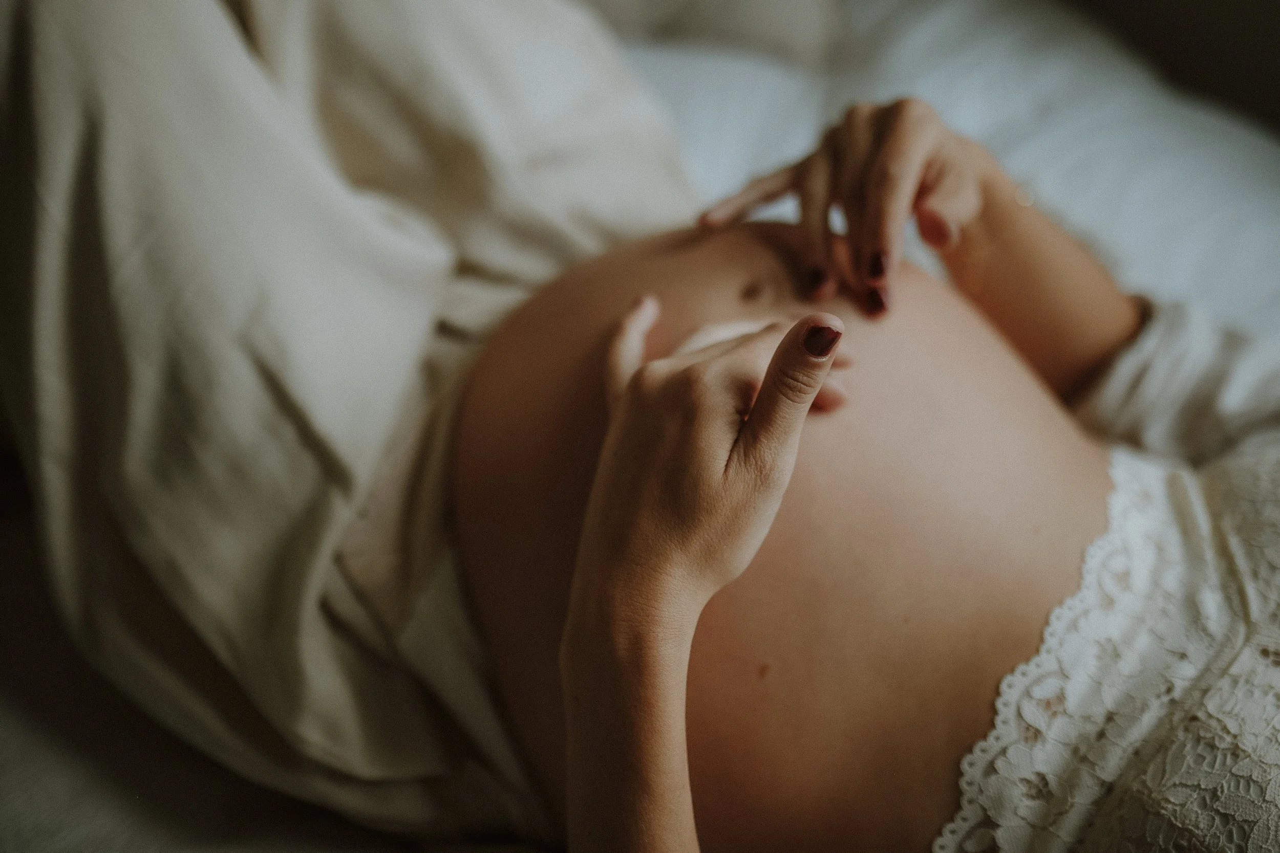A pregnant woman lying in bed, gently touching her baby bump with one hand and resting her other hand on her stomach.