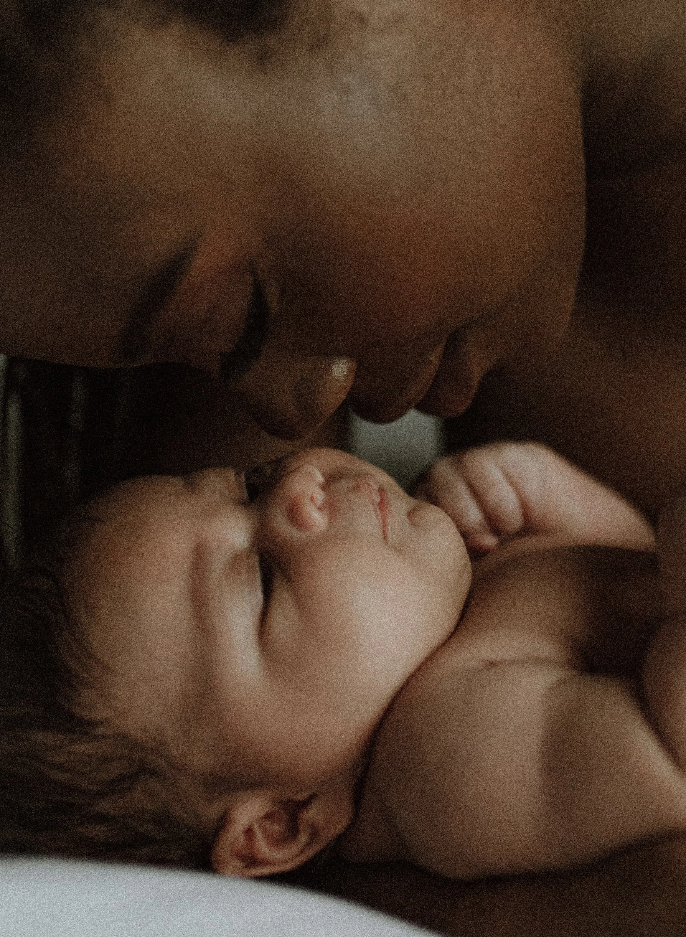 An adult man gently touching foreheads with a sleeping baby, close-up shot.