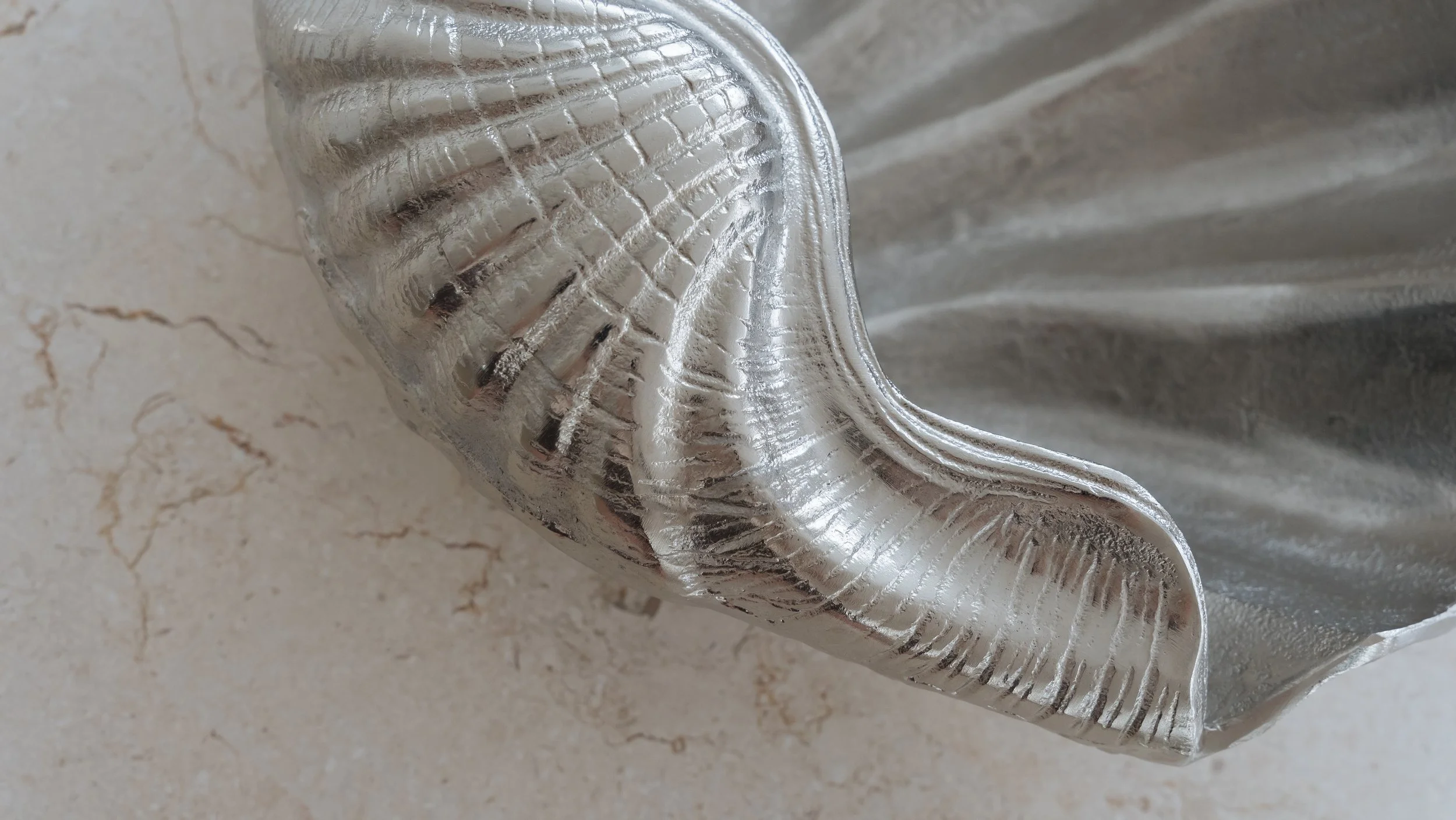 A close-up view of a crumpled, reflective silver foil packet on a light-colored textured surface.