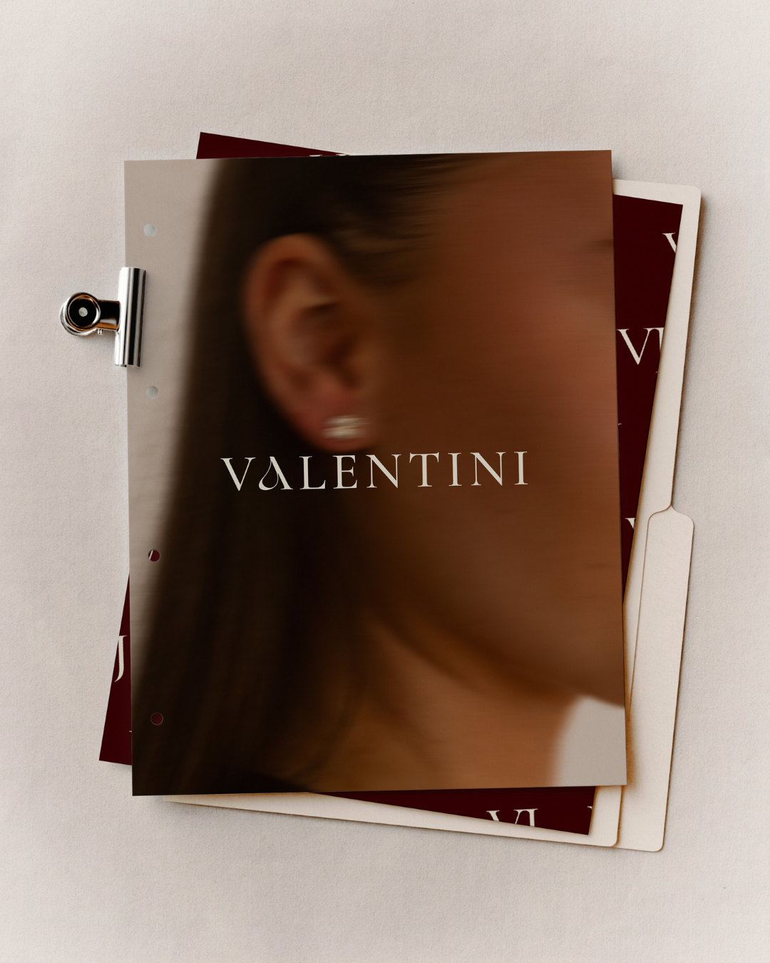 A magazine or brochure with a blurred photo of a woman wearing pearl earrings, displaying the word 'Valentini' on the front, clipped on a white background.