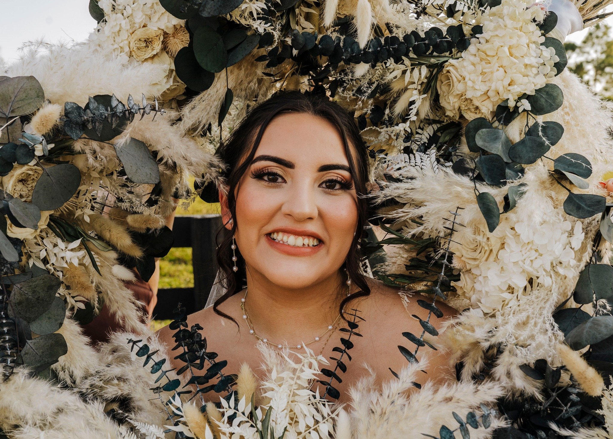 Closeup photo of bride by a fence a with all her bridesmaids holding a bouquet of flowers close to her head. 