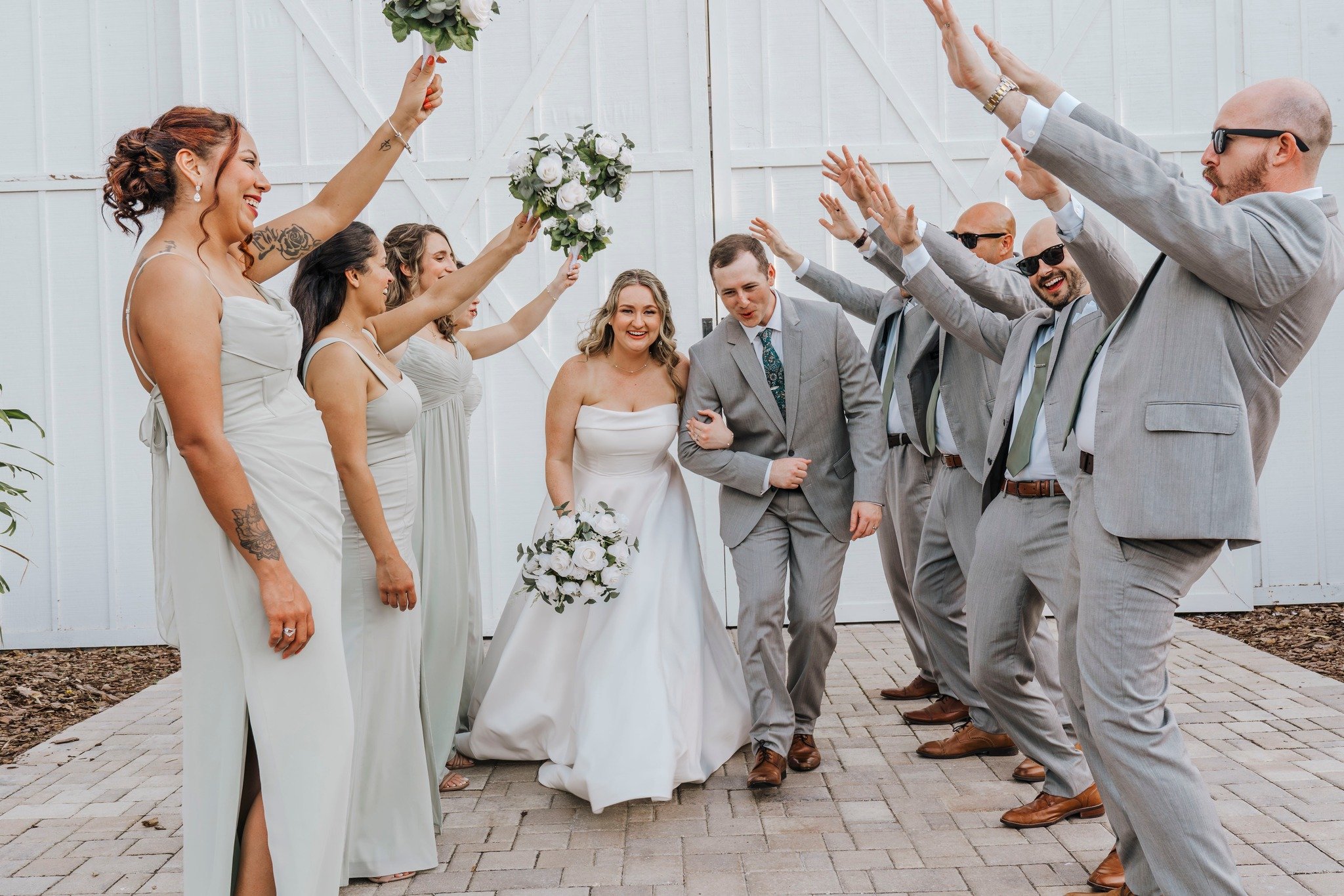 Newlywed couple walking though a man made arch. Bridesmaids and groomsmen have their hands up for them to walk under.