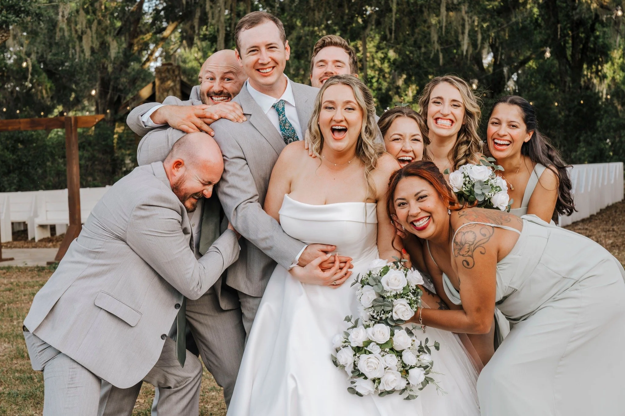 Wedding party surprising bride and groom with a surprise hug. Bride is smiling and grateful for the memories captured. 