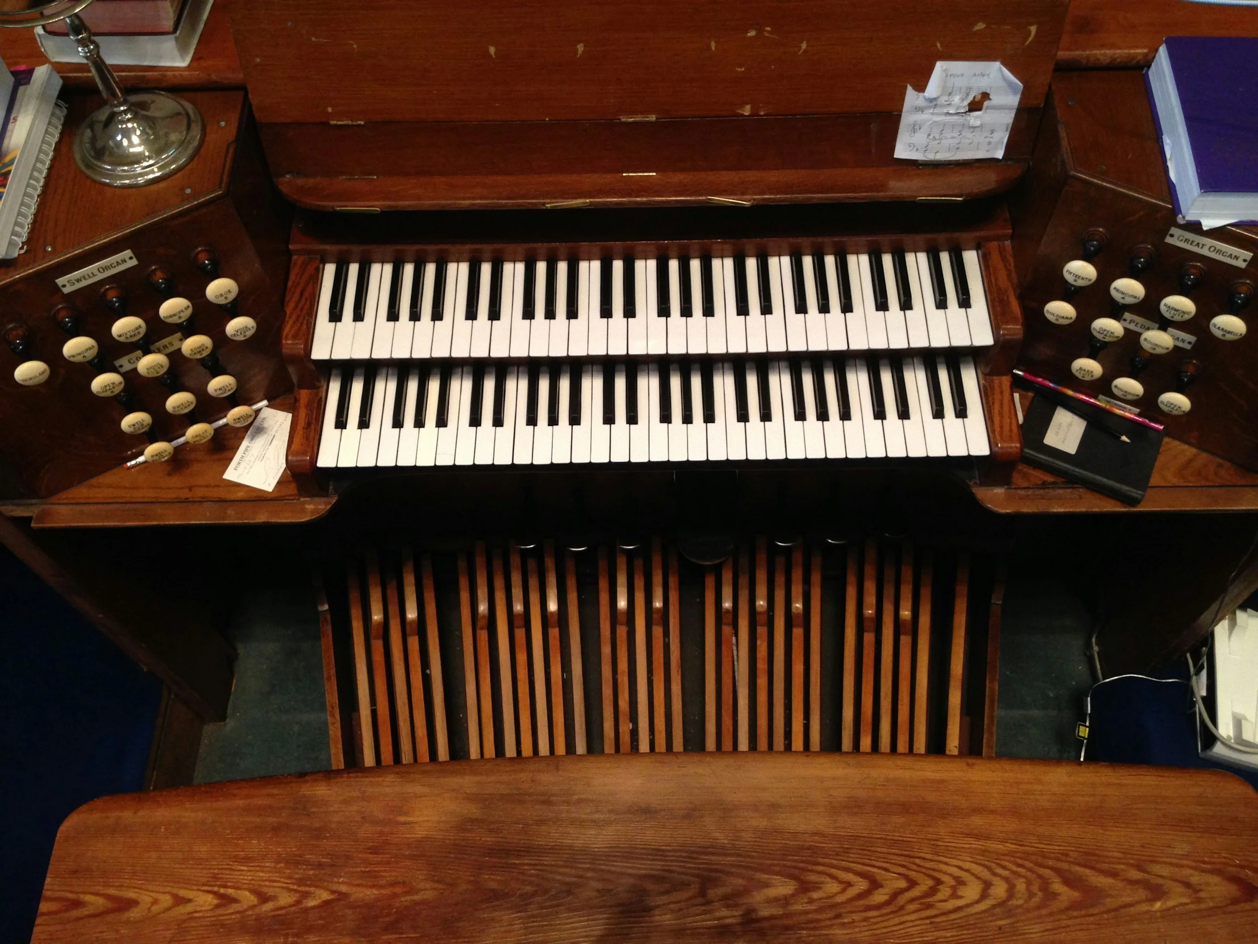 A vintage wooden pipe organ with black and white keys, labeled stops on the side, and sheet music on top.