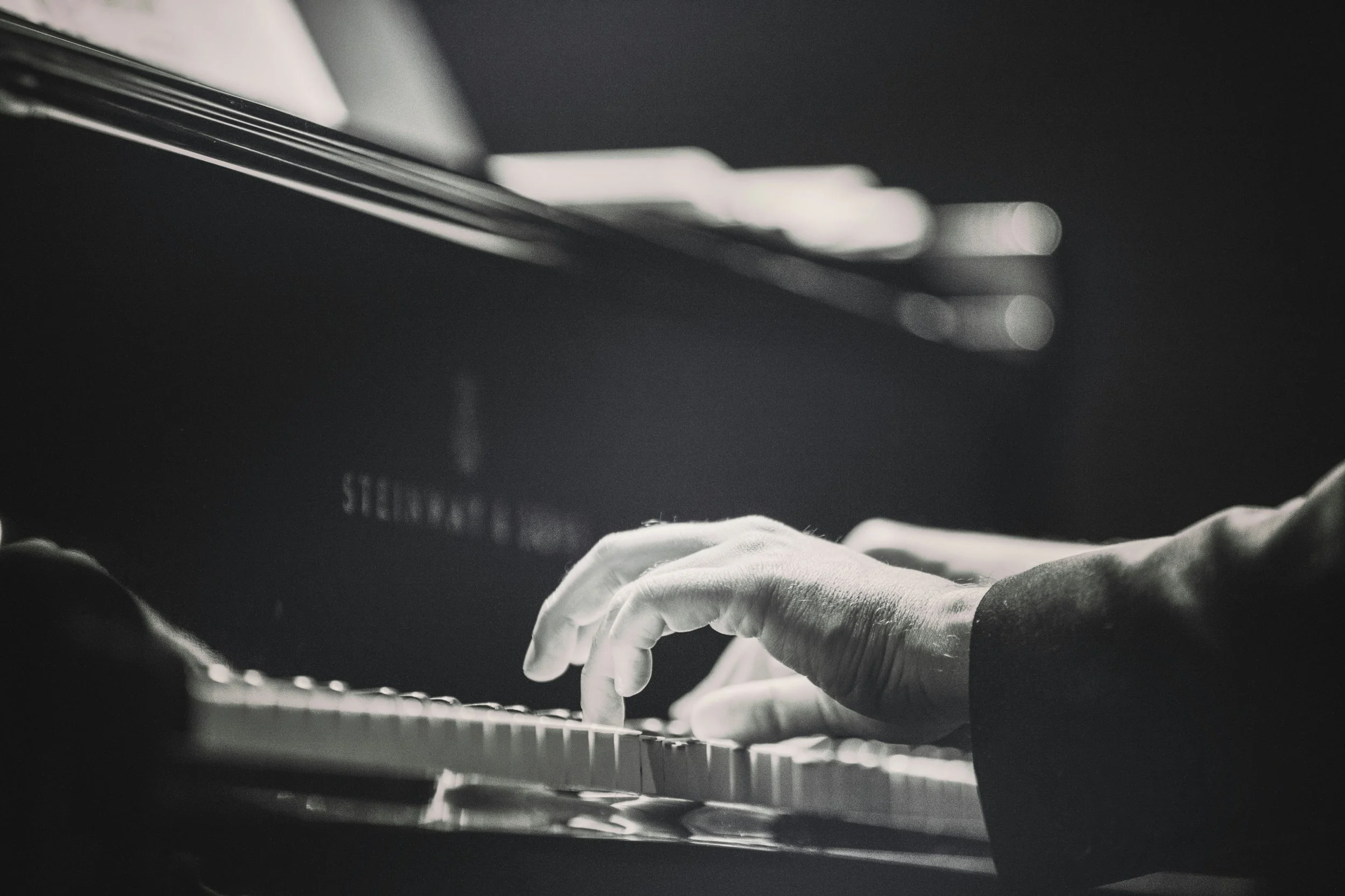 Close-up of a person's hands playing the piano, wearing gloves, with focus on the keys and the person's fingers.
