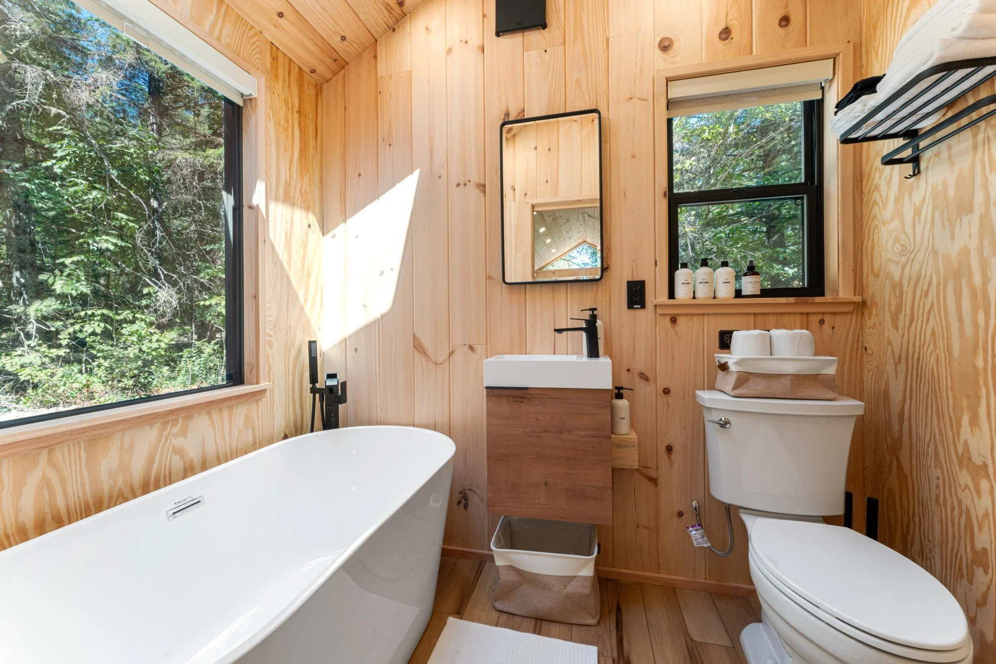 Modern bathroom with large picture window, soak tub, flush toilet, small vanity, and white pine walls.