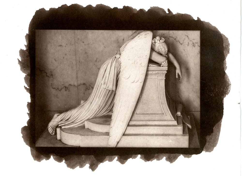 A Salt Print of a photograph of a classical marble sculpture of a fallen angel, lying on a pedestal, with large wings, a long draped garment, and a dejected pose, surrounded by a dark irregular border.