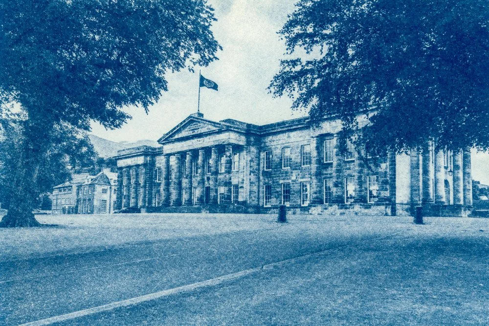 A cyanotype print of the Senior School building at Dollar Academy, a Scottish Independent school, with tall columns, surrounded by trees, flying the school flag on top.