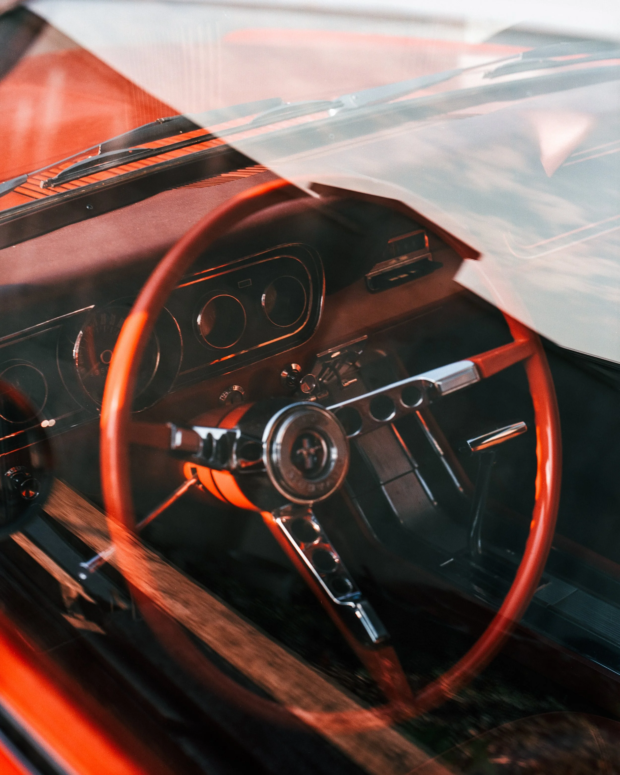 Close-up of a vintage car's interior seen through the windshield, featuring a retro dashboard and a red steering wheel.