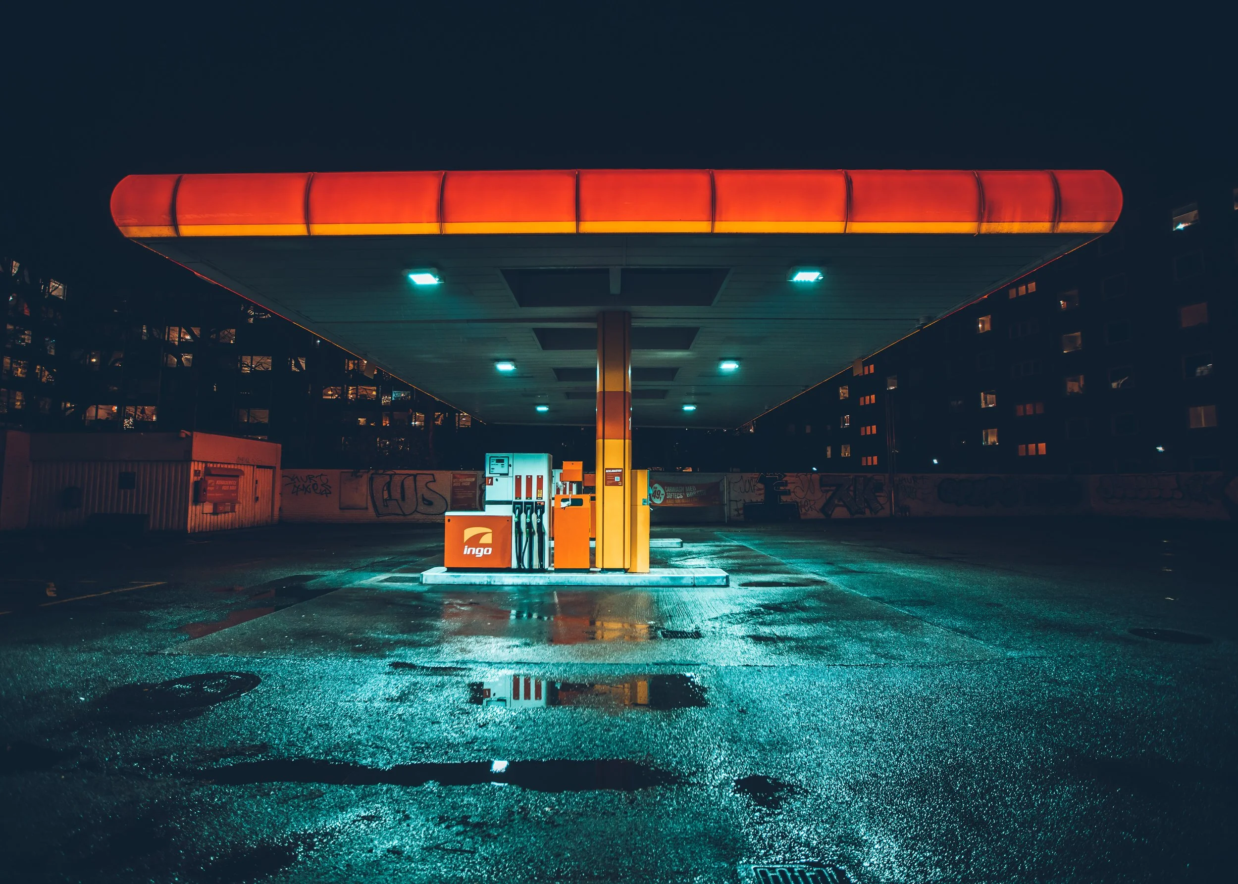 Empty gas station at night with wet pavement reflecting the station's lights.