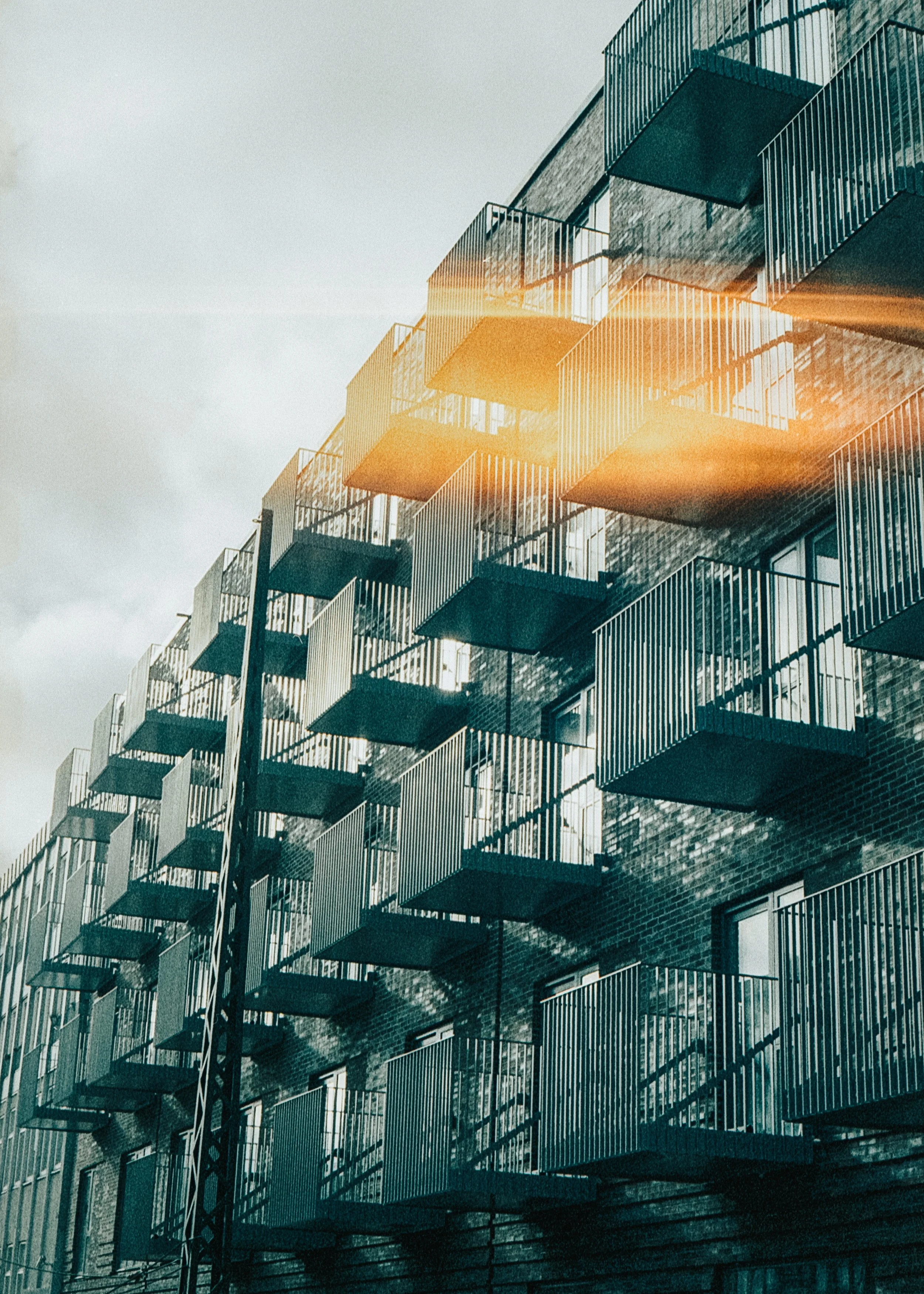Multiple apartment units with balconies on a brick building, with sunlight reflecting off some balconies.