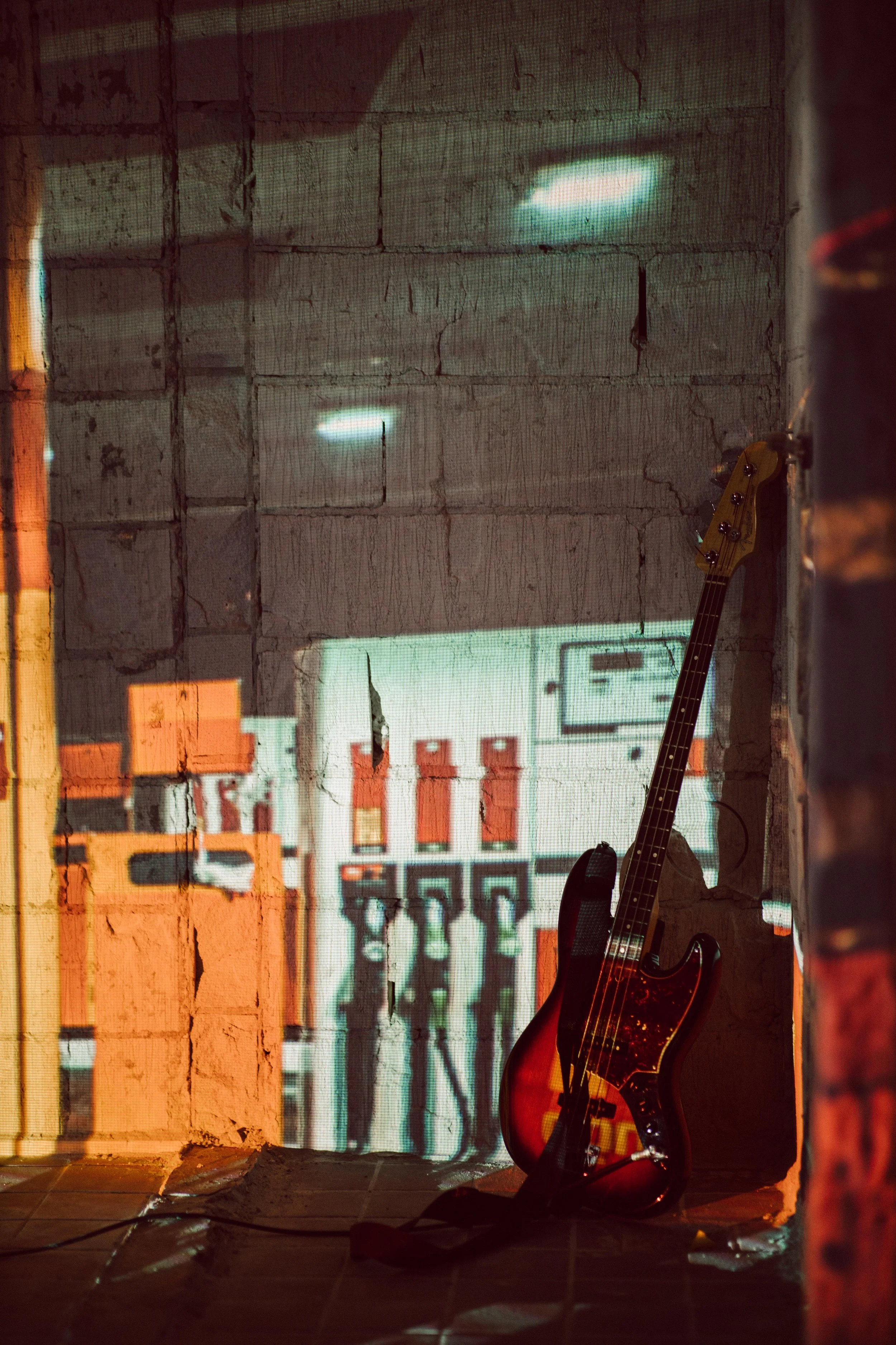 Electric guitar leaning against a rustic brick wall with a projection of gas pumps and a sign in the background.