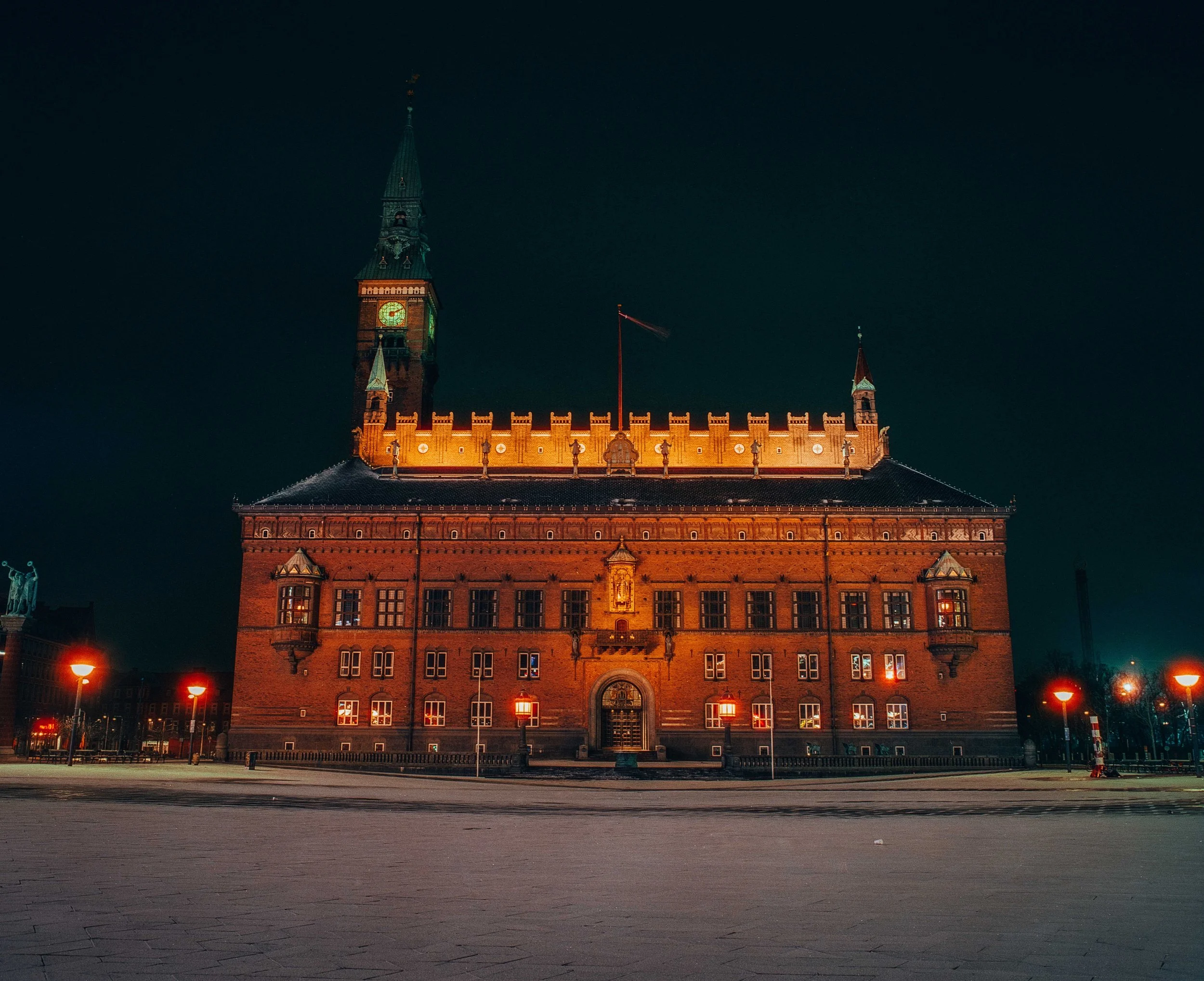 Night view of a historic brick building with a clock tower, illuminated with warm lighting, in a city square.