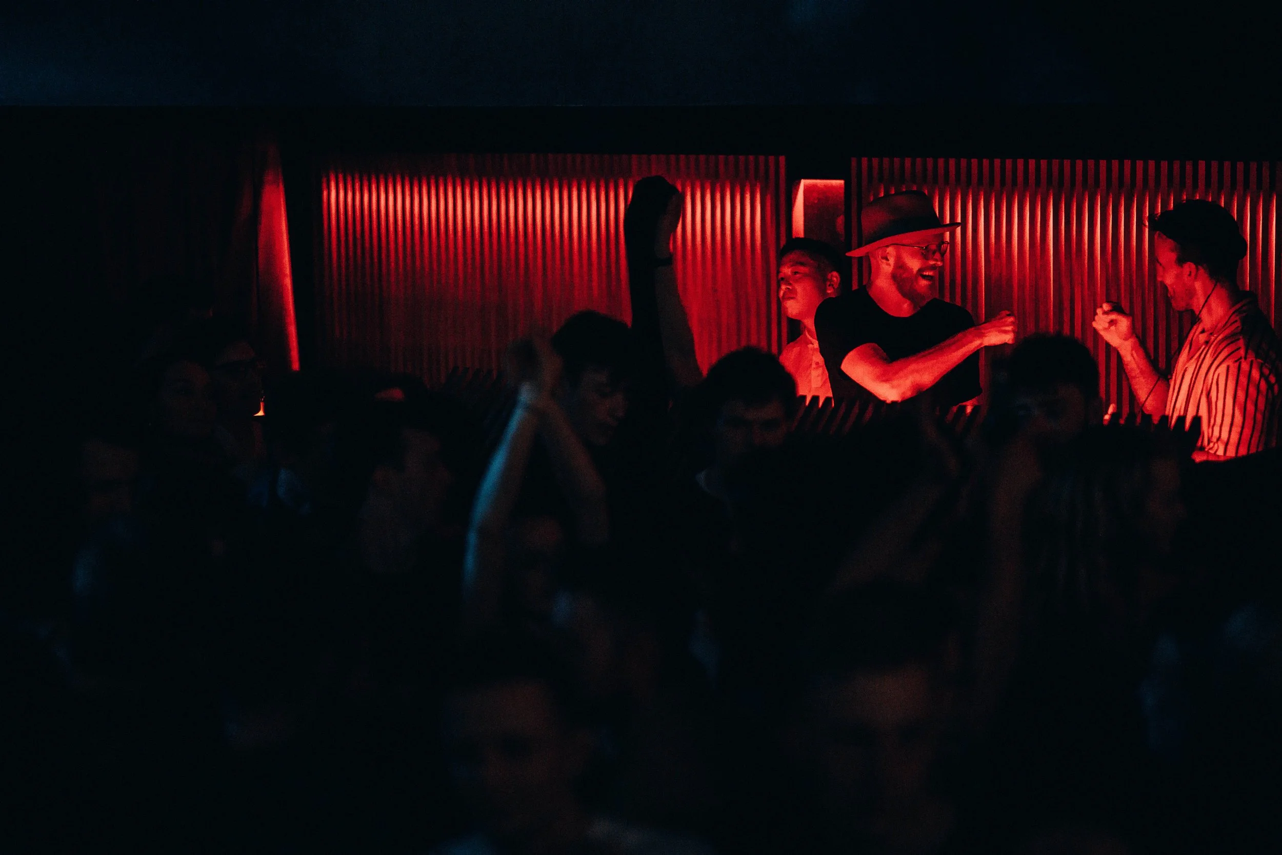 People dancing and socializing in a dimly lit nightclub with red lighting and a lively atmosphere.