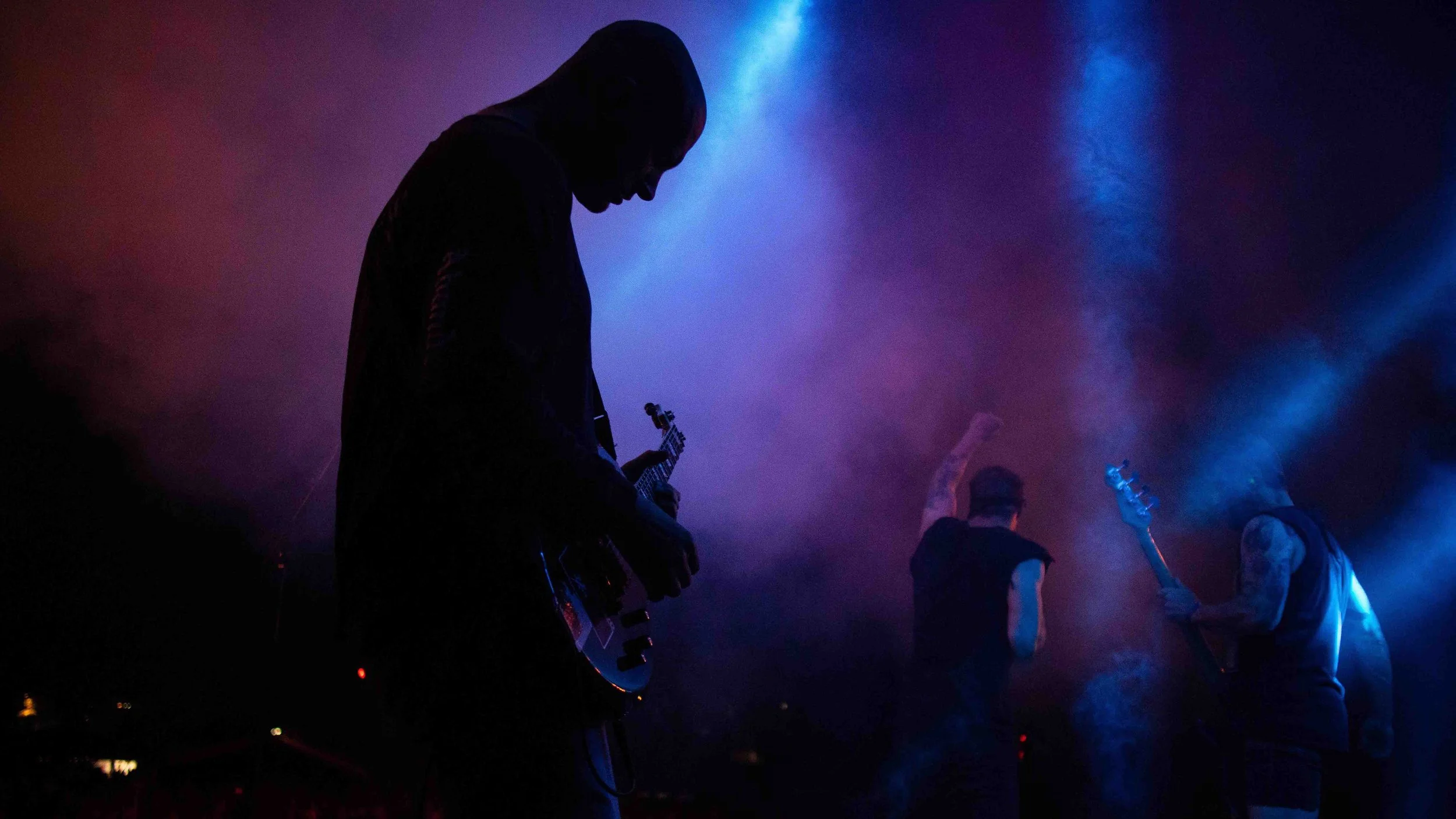 Silhouettes of four musicians playing guitars on stage with colorful blue and purple lighting.