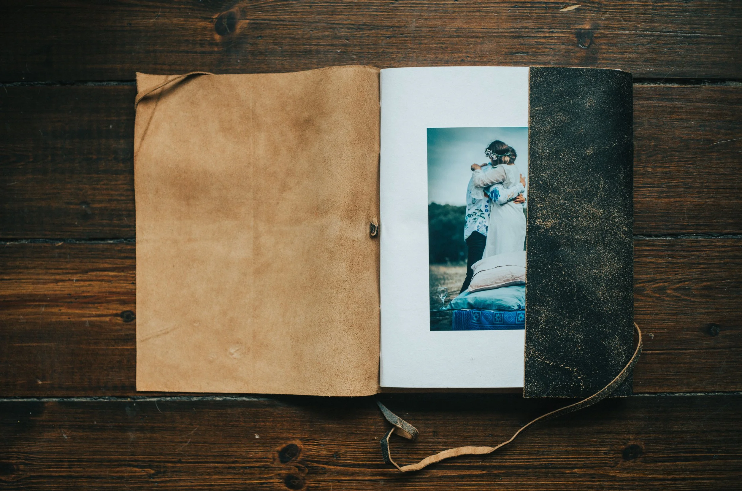 An open photo album with blank pages and a small photo of a couple hugging, placed on a wooden surface.