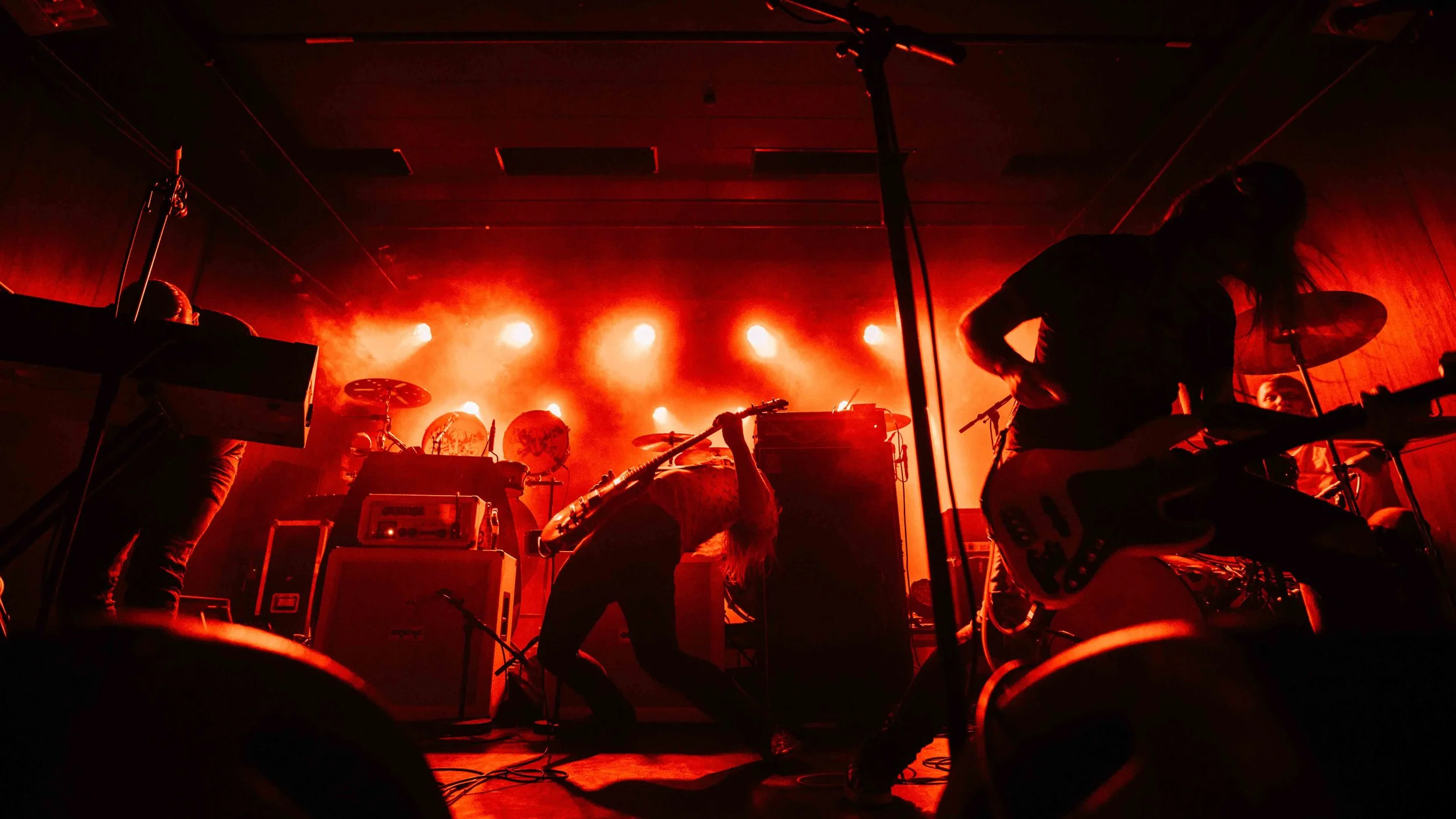 Silhouettes of band members performing on stage with red backlighting and musical instruments.
