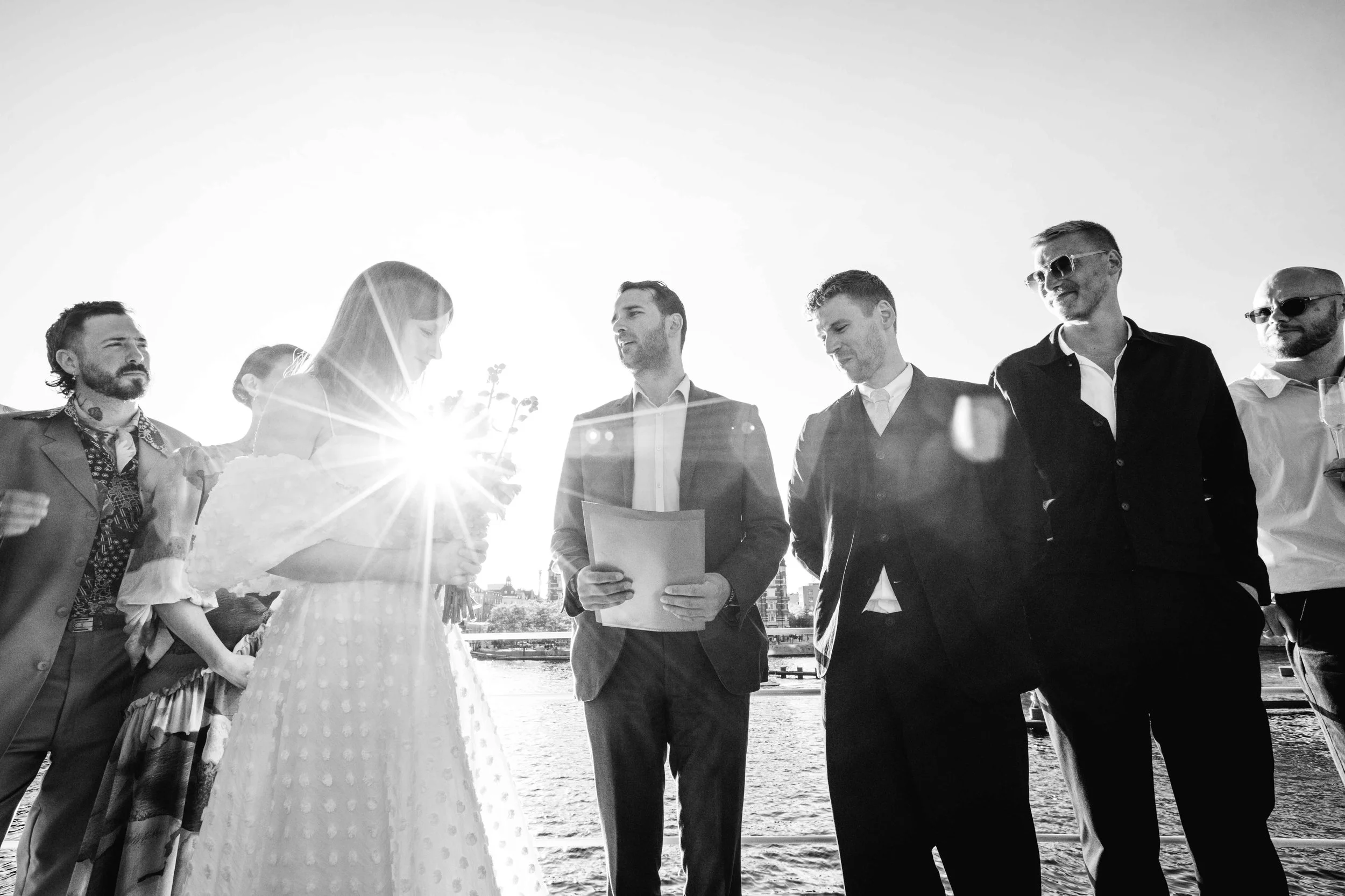 Couple getting married outdoors by a river with officiant and guests, black and white photo
