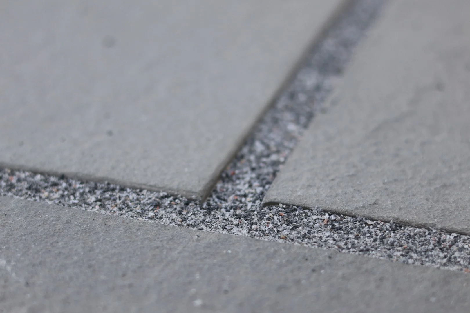 Close-up of a concrete sidewalk with a crack filled with small gravel and sand.