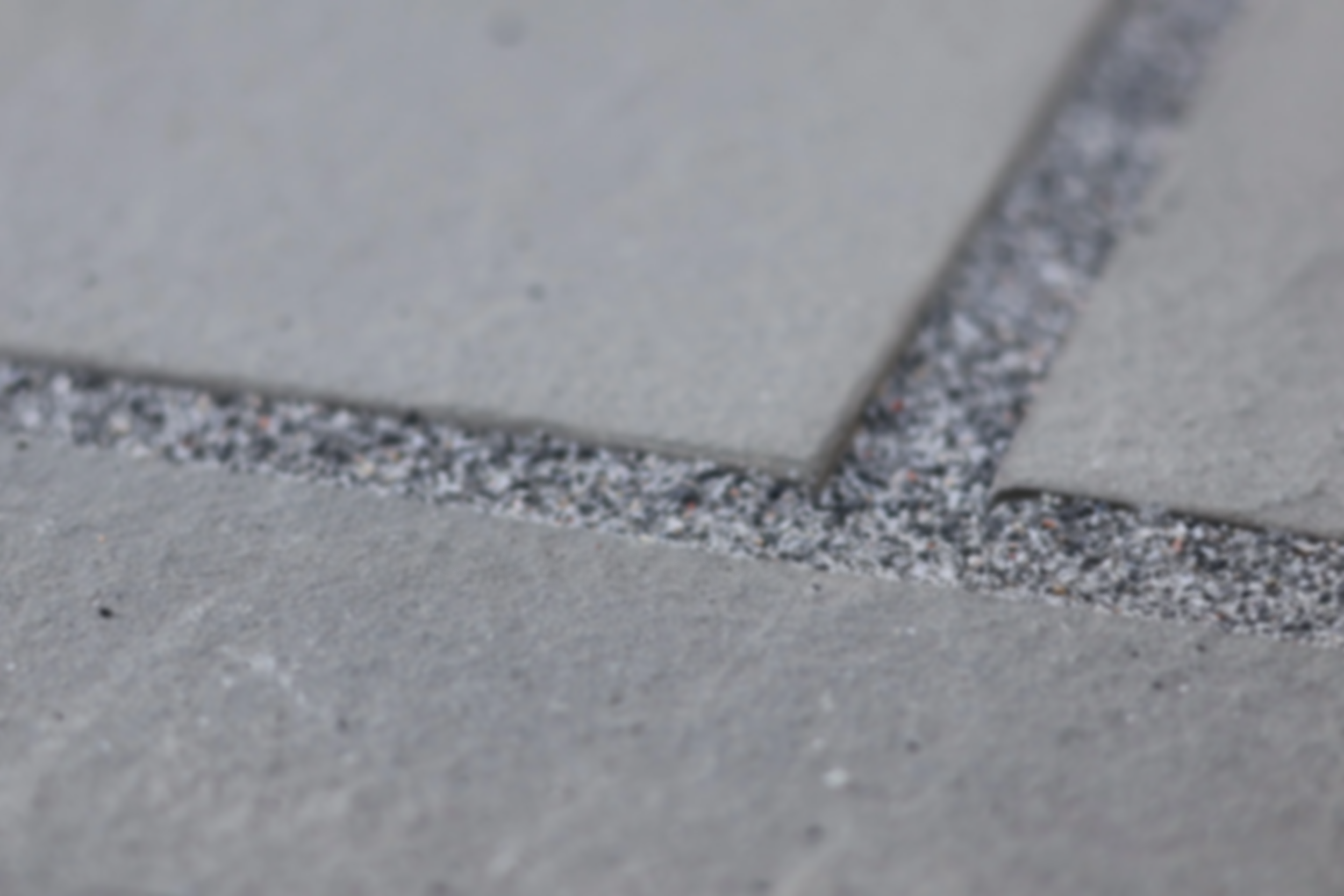 Close-up photo of gray concrete sidewalk with a crack filled with small gravel and tiny stones.