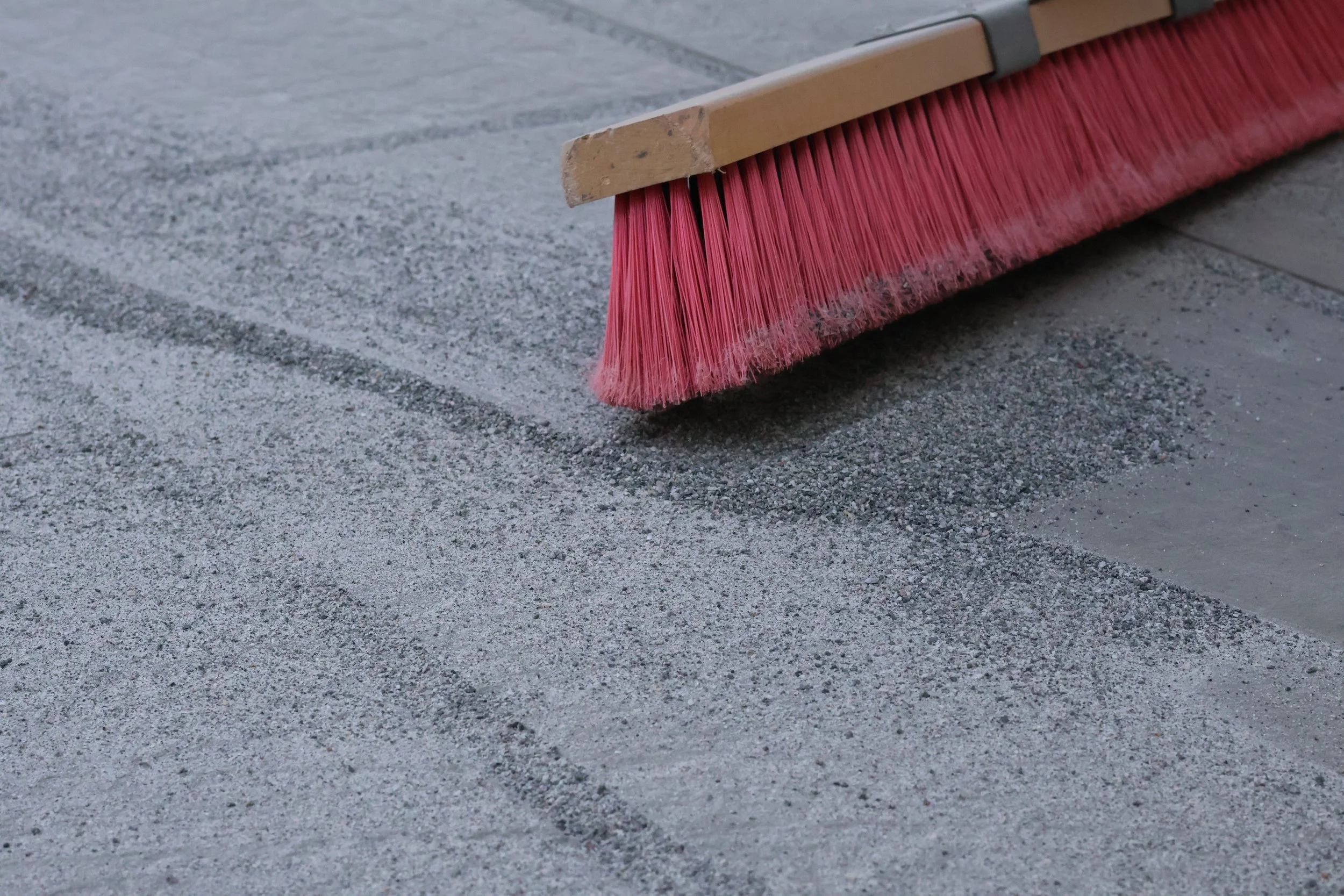 A worker sweeping freshly laid bricks outside a building with wooden siding.