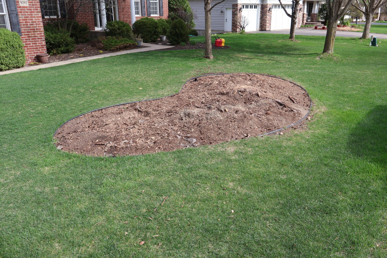 A front yard with green grass and a large oval-shaped area of soil, surrounded by a black edging border, likely for planting or landscaping.