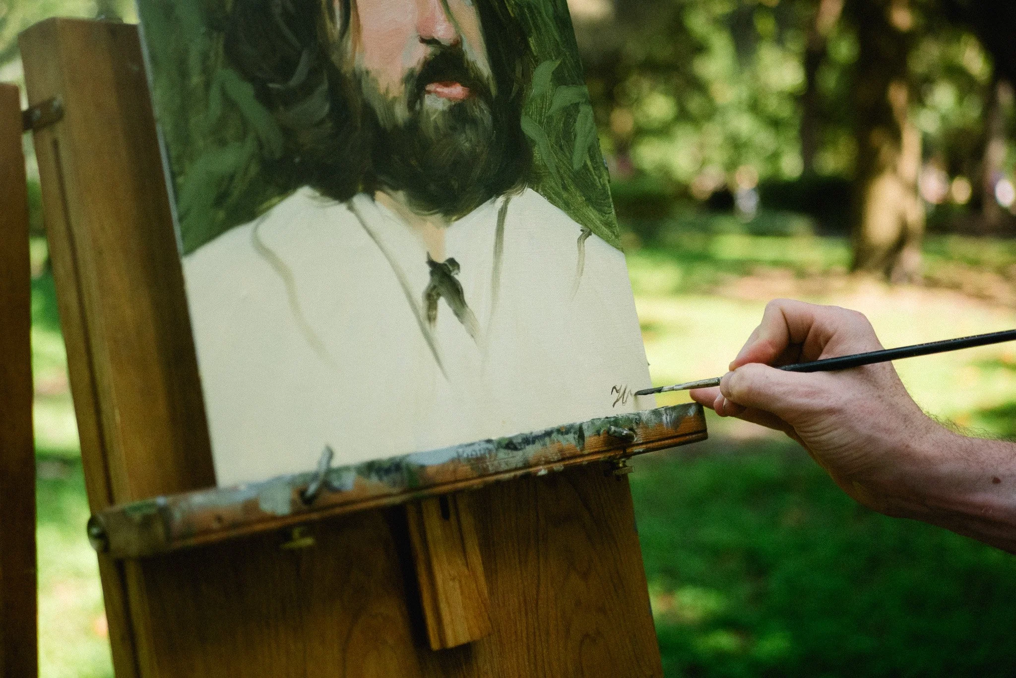 artist signing finished oil portrait painting on easel in outdoor setting