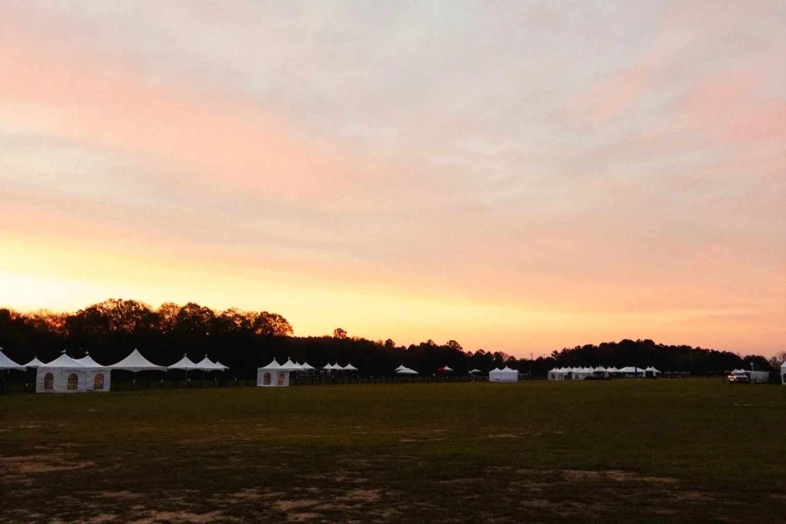 Sunset over the Aiken Steeplechase Racecourse grounds, white event tents silhouetted against a warm spring sky