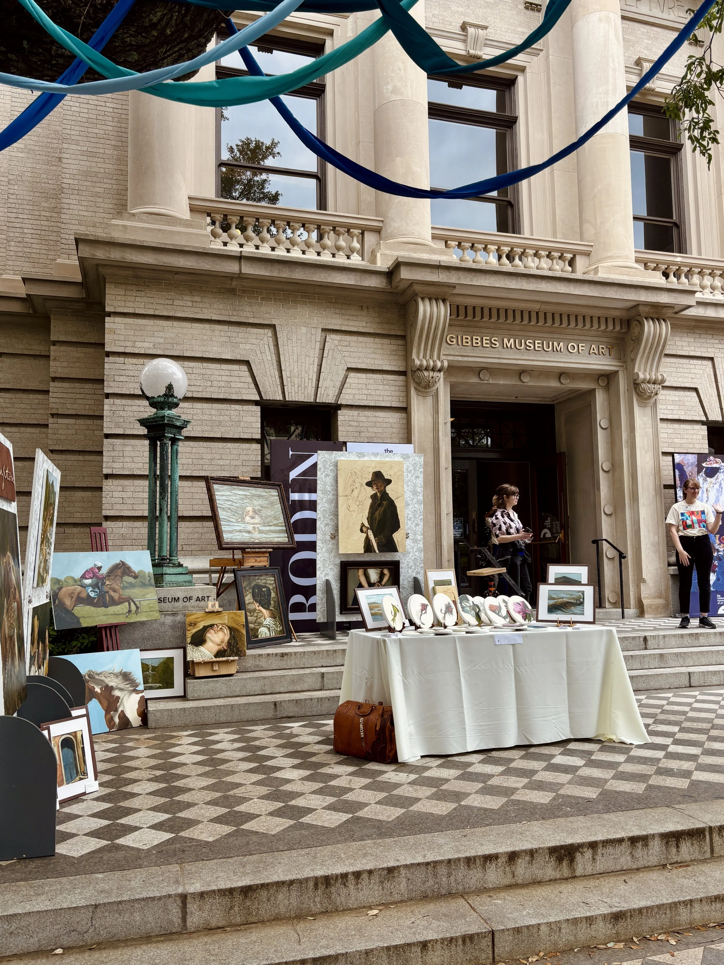Artists displaying work on the front steps of the Gibbes Museum of Art during Art Charleston, with paintings leaning against the neoclassical stone facade on Meeting Street