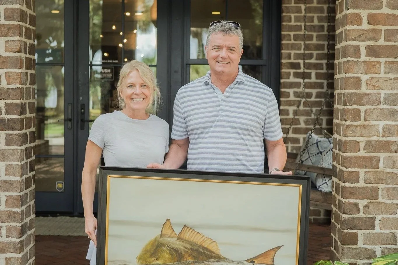 Two collectors holding Breaking the Plane, a 24x36 oil painting of a redfish breaking the surface, outside Flow Gallery + Workshop at Palmetto Bluff