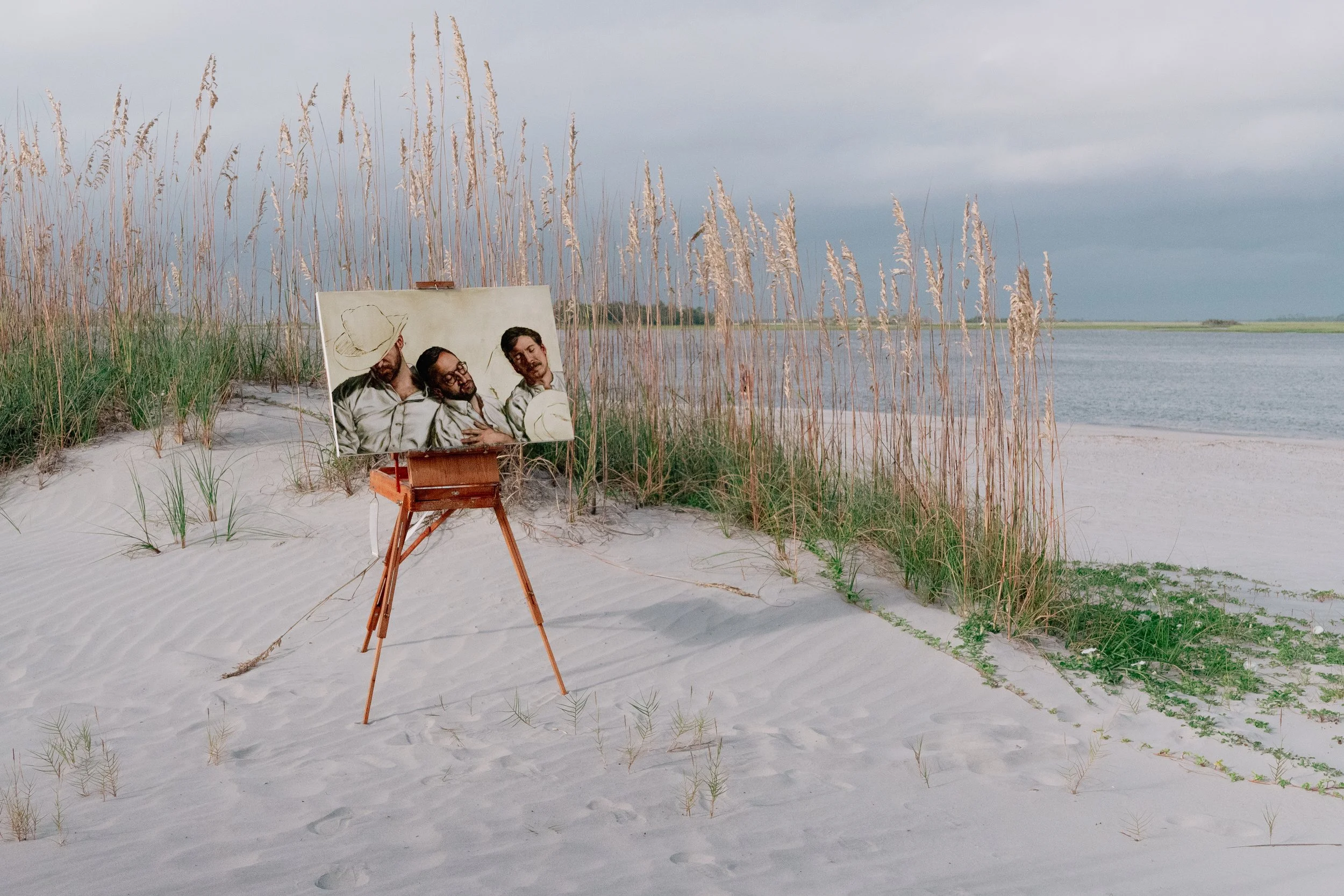 Figurative oil painting of three men displayed on easel in Tybee Island dunes