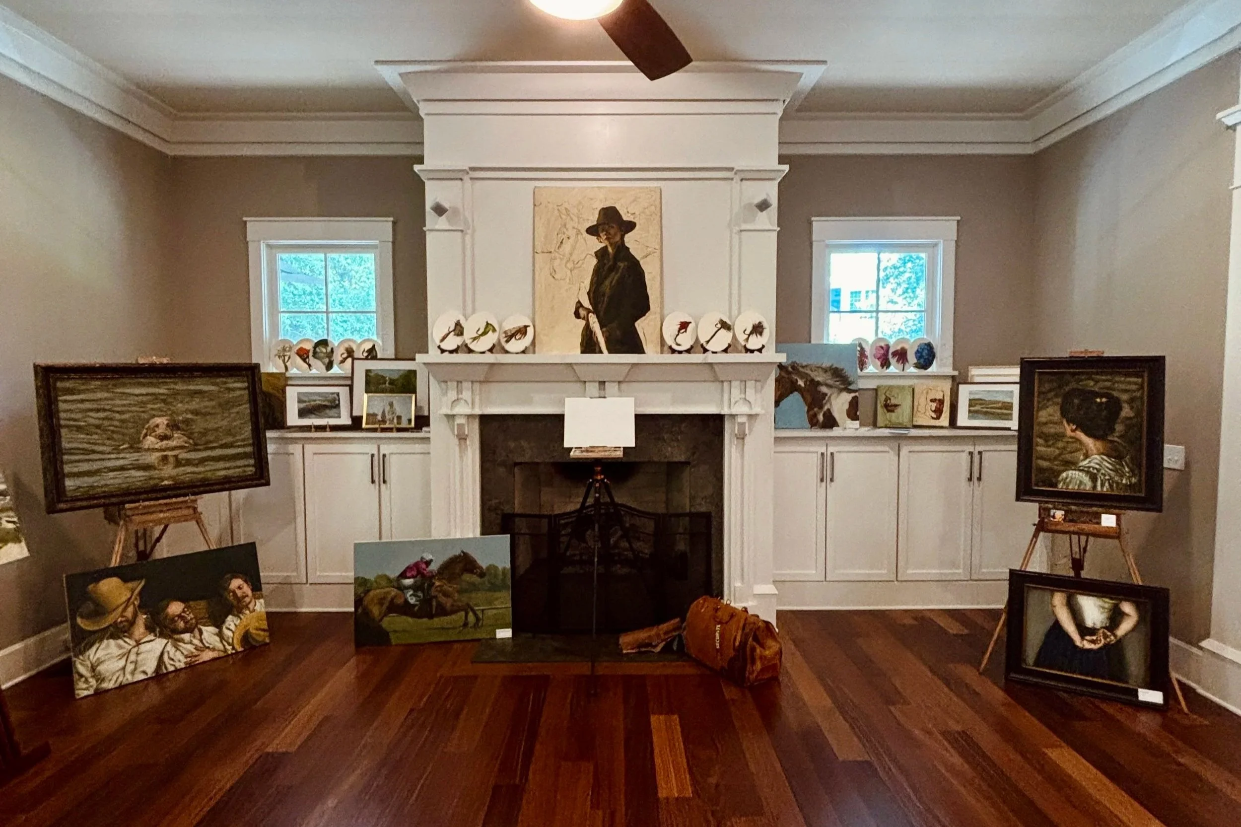 Interior salon exhibition of Hampton Watts oil paintings at Art I'ON in Charleston, with works including portraits, equestrian scenes, sporting subjects, and wildlife displayed on easels around a fireplace room with warm hardwood floors