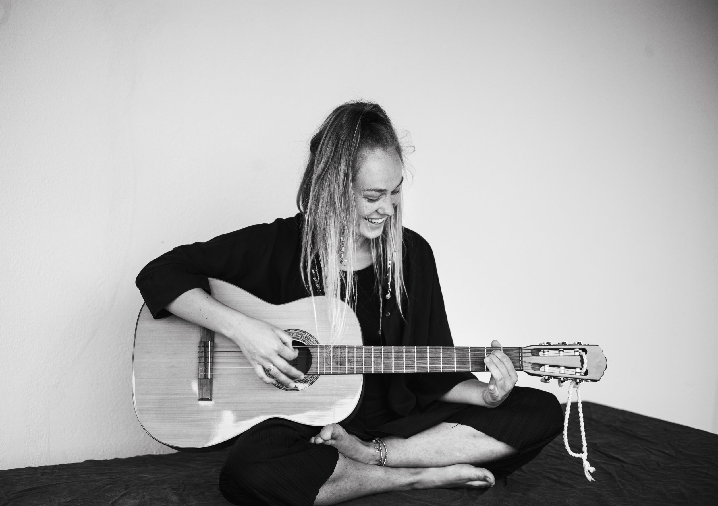Katharina Wirth sitting, smiling and playing the guitar. Black & White Colors. Sexological Bodytherapy.