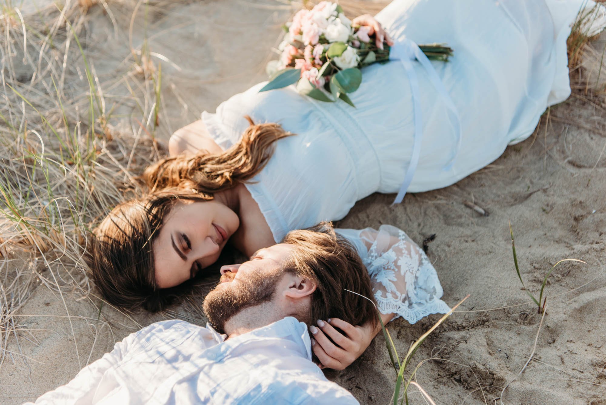 Eloping couple lies in the grass near the ocean before saying their vows. Visit www.loveplustravel.com to book your elopement photographer.
