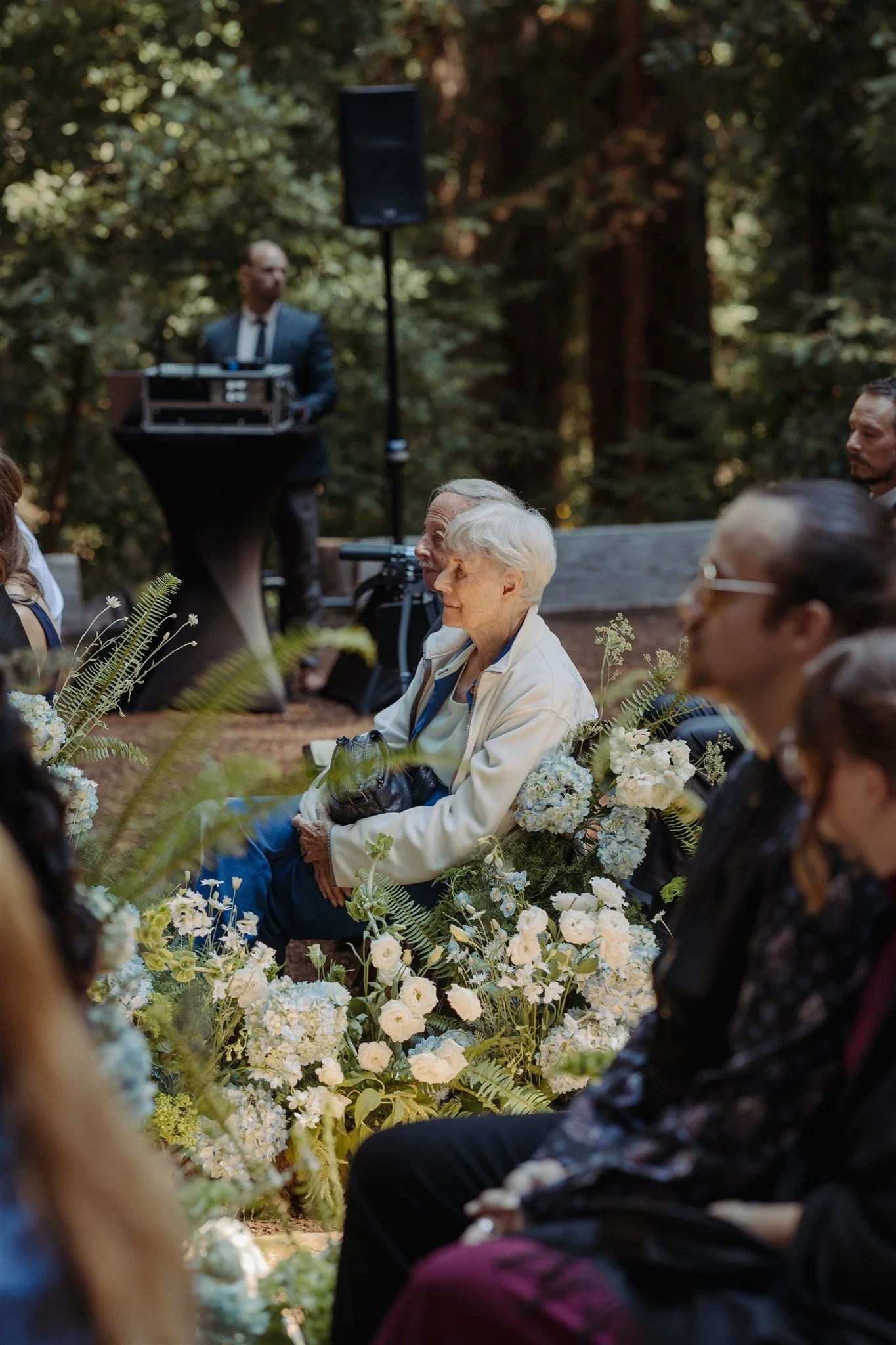 older woman wedding guest watching wedding with tall flowers showing