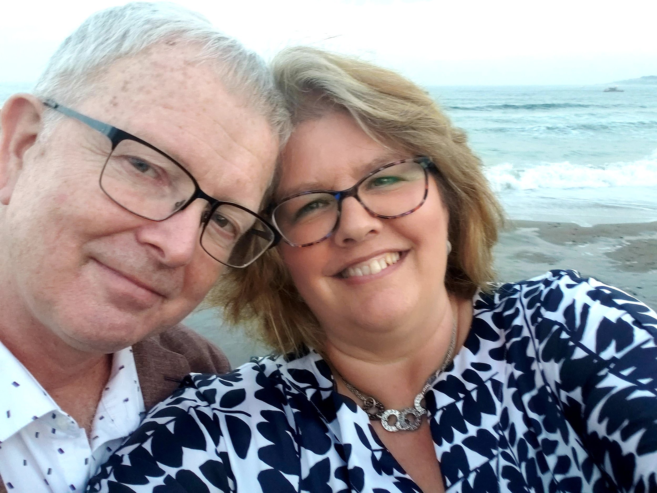 A smiling couple taking a selfie on the beach with the ocean in the background.