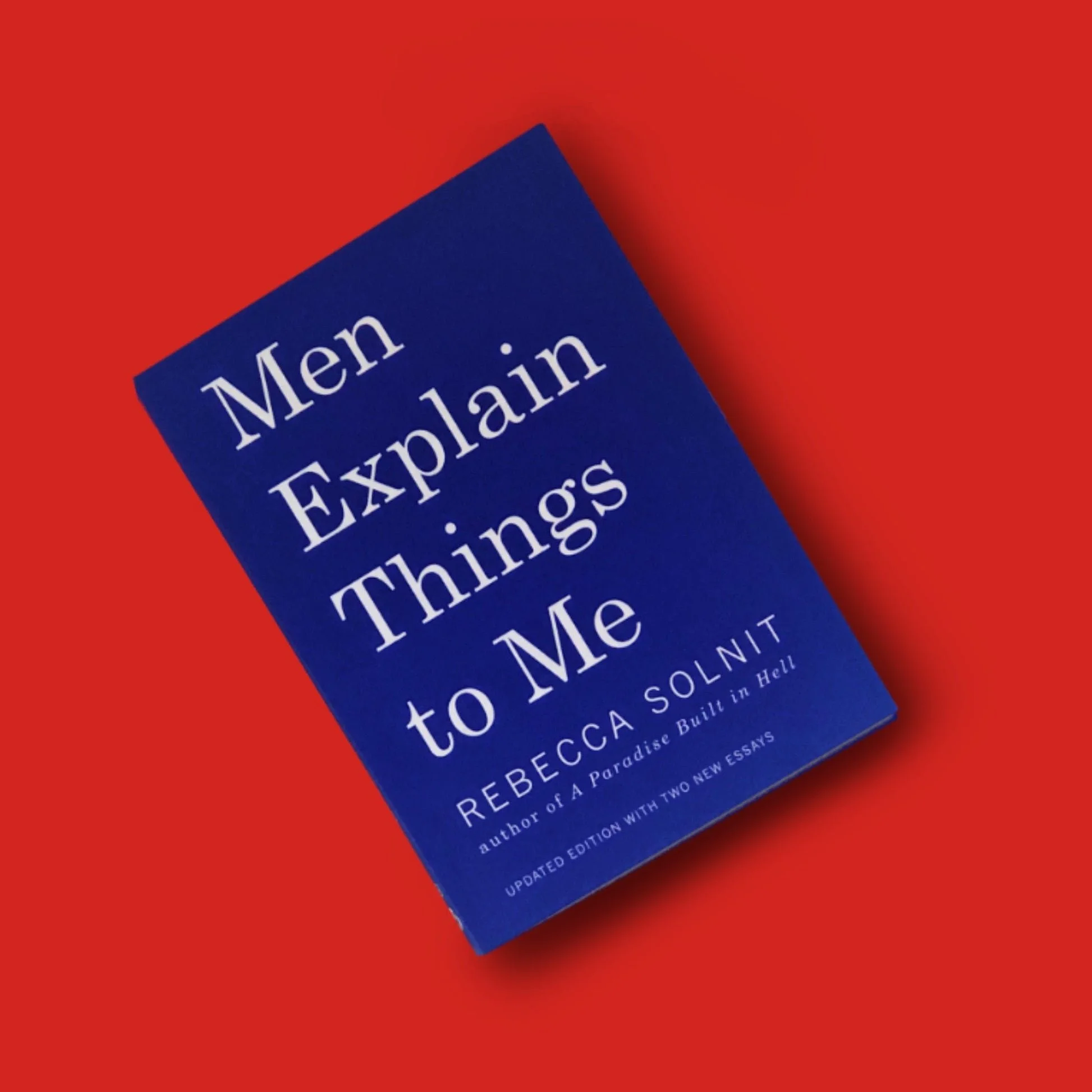 A blue book titled 'Men Explain Things to Me' by Rebecca Solnit on a red background.