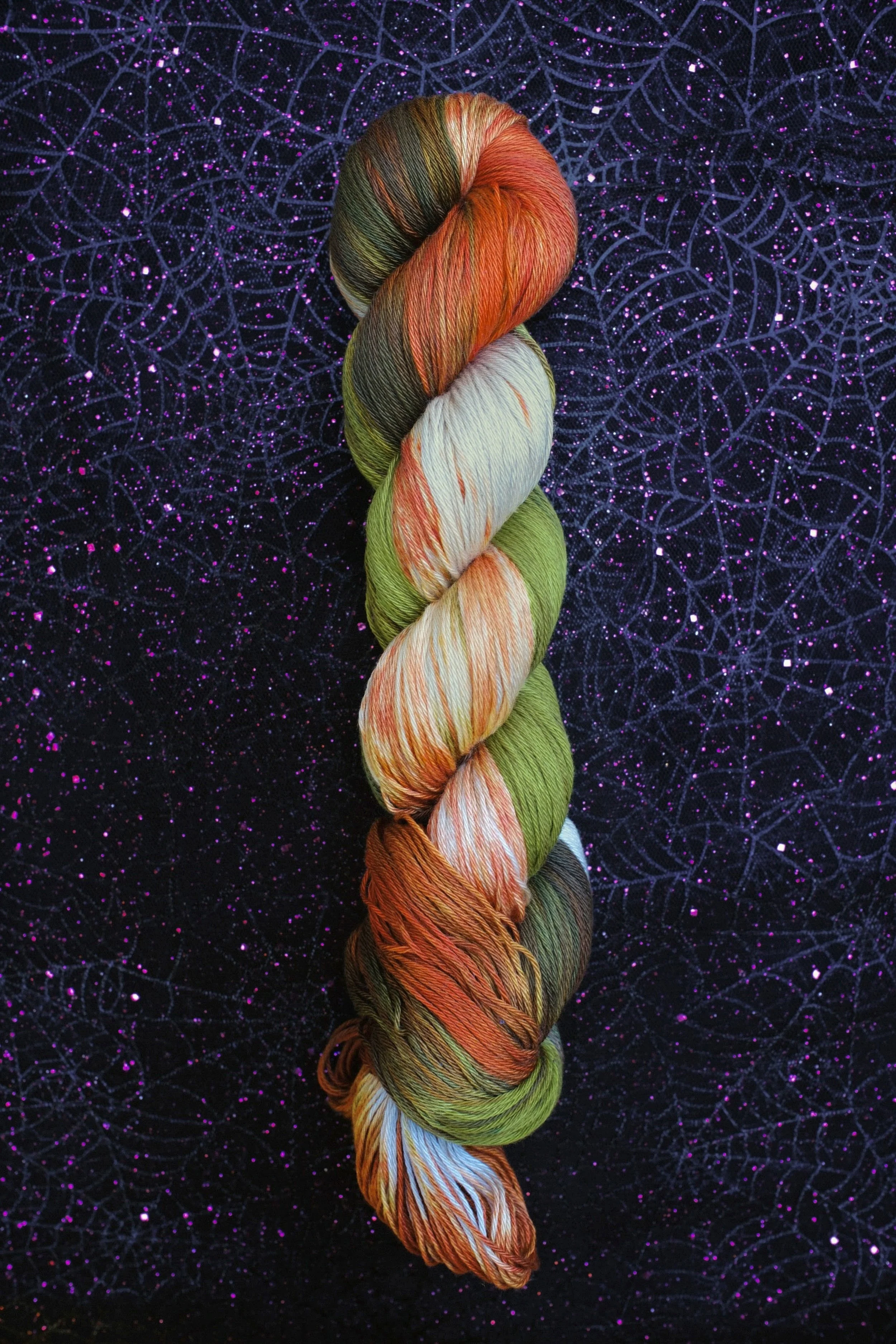 Colorful skein of yarn on a purple glittery spiderweb background.