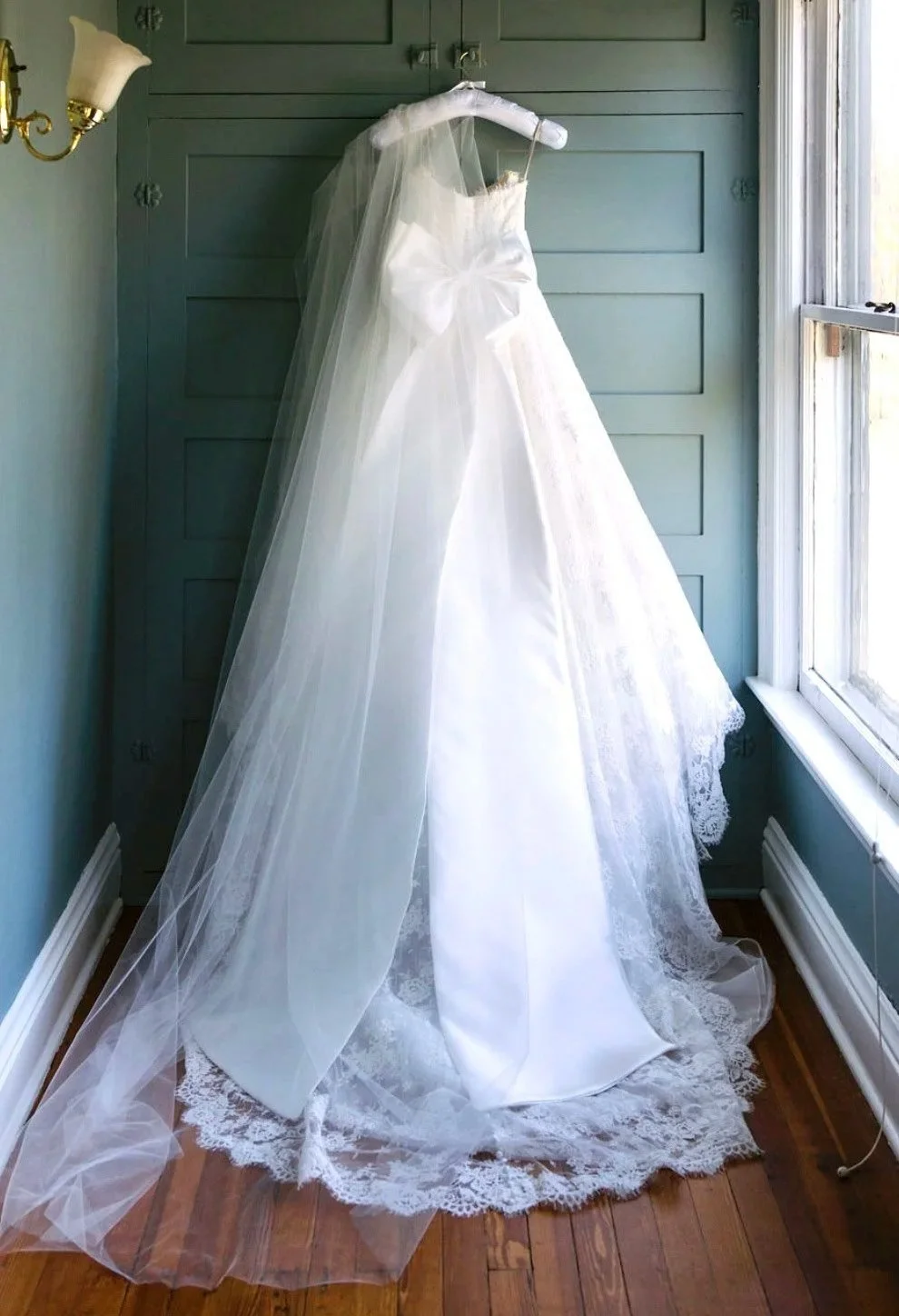 Client photo of white wedding gown hung on white satin wedding dress hanger, custom hanger, with personalized embroidery by the boondock quilt co